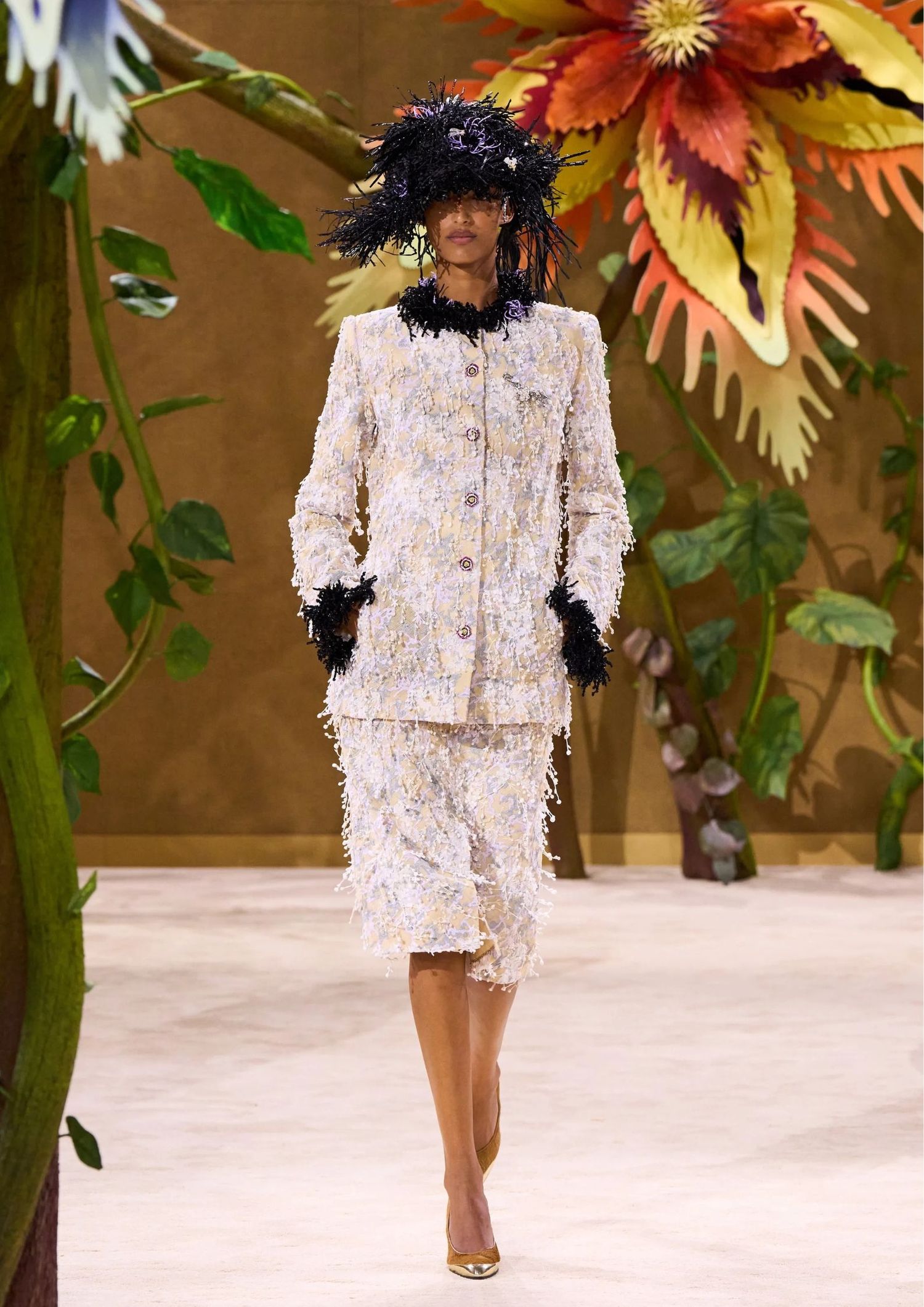 Textured tweed jacket, with a matching midi skirt, a black feather-trimmed hat, and metallic pointed-toe heels