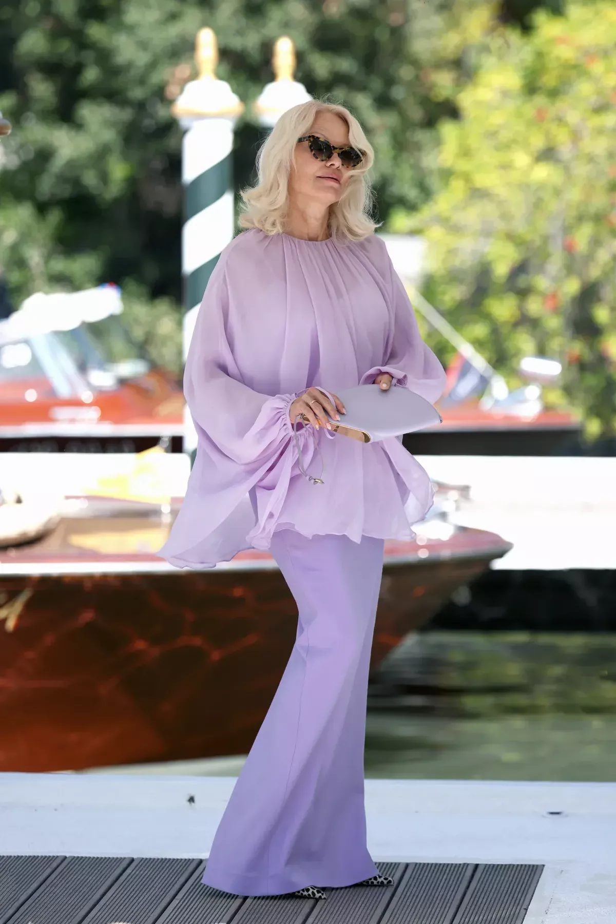 Pamela Anderson stands on the dock at the Venice Film Festival wearing a lilac two piece and black sunglasses