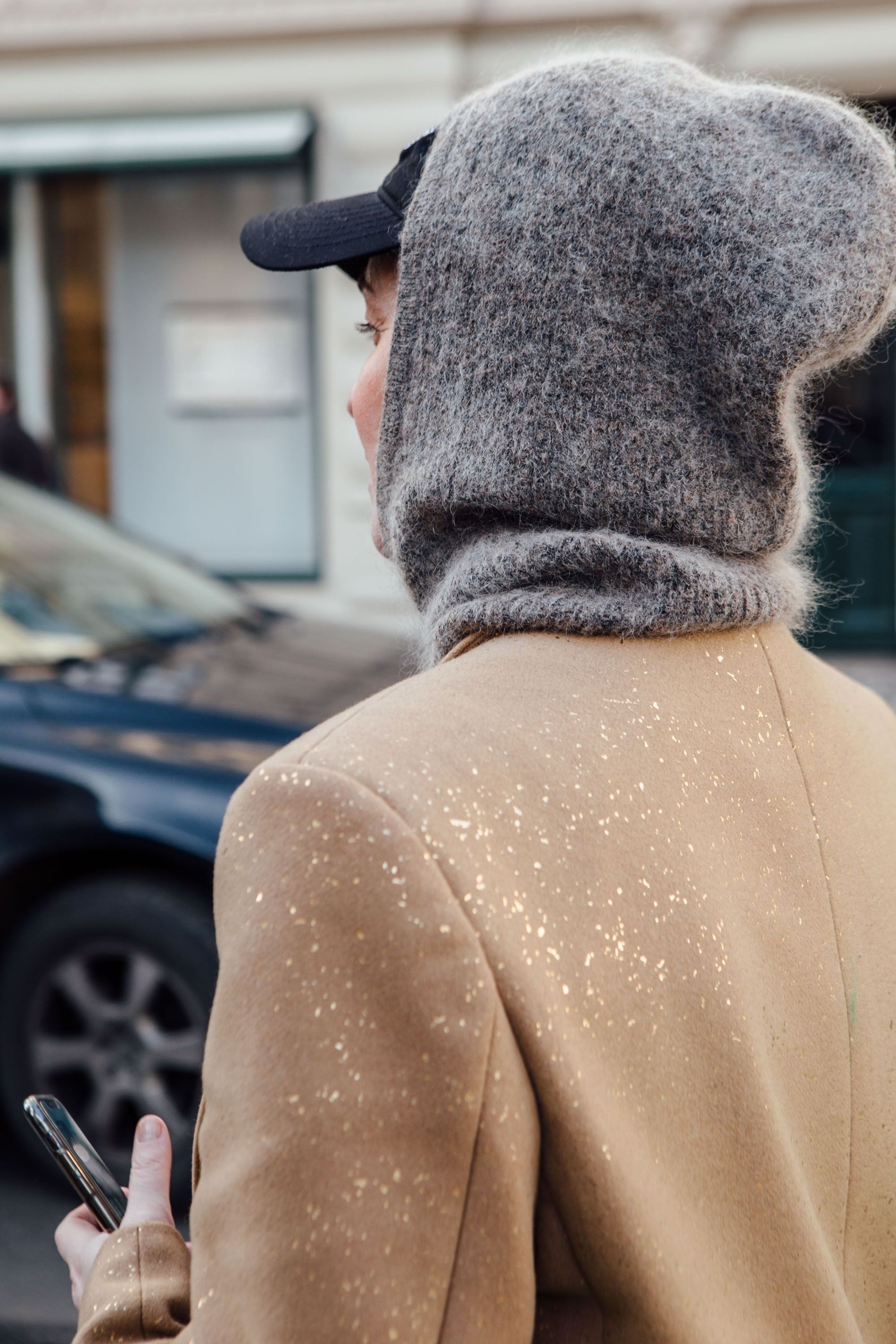 A Copenhagen Fashion Week guest wears a grey fuzzy balaclava, black cap and beige coat