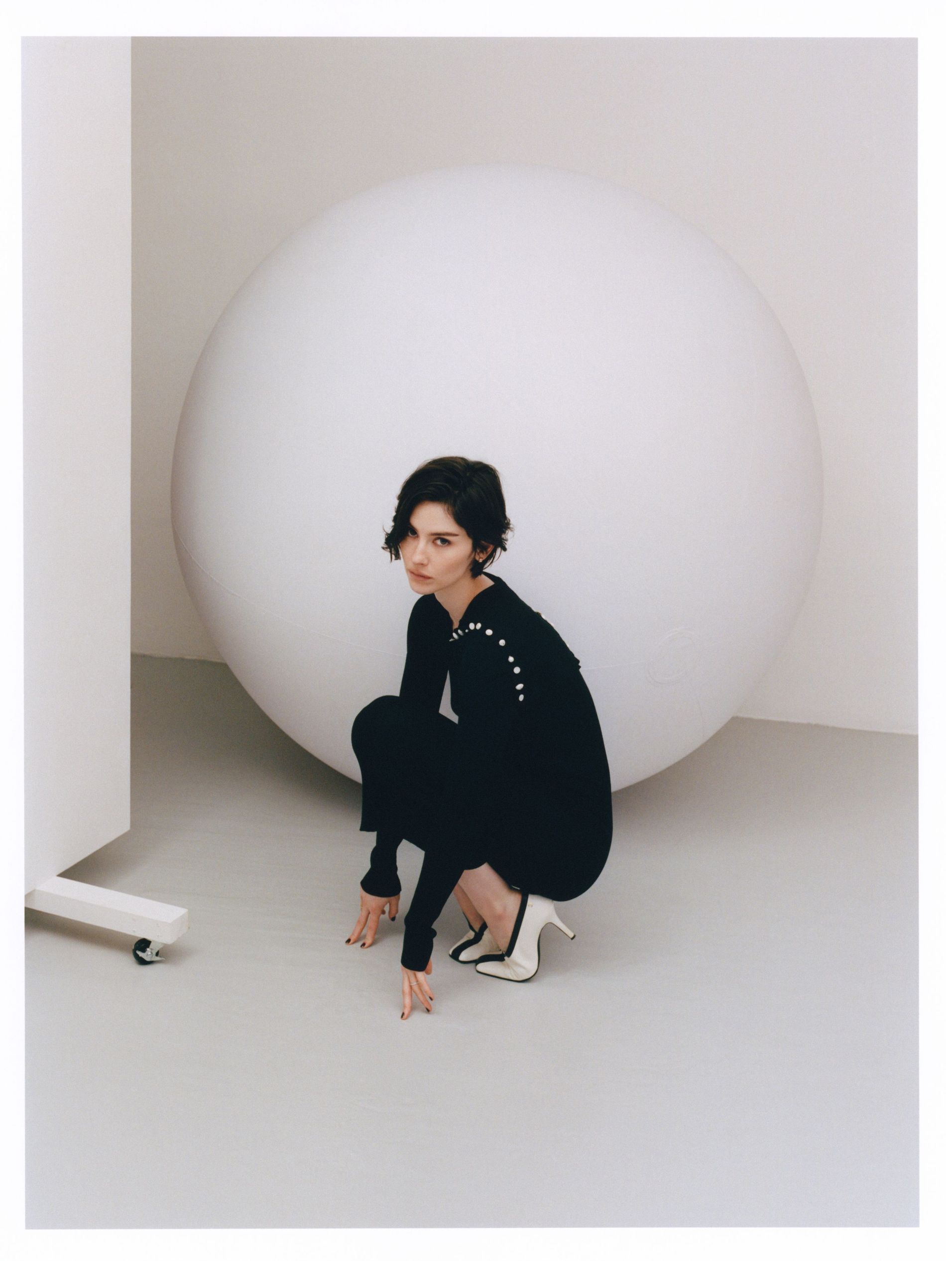 Garcie Abrams poses in a black knitted dress on a white soundstage with black and white pumps