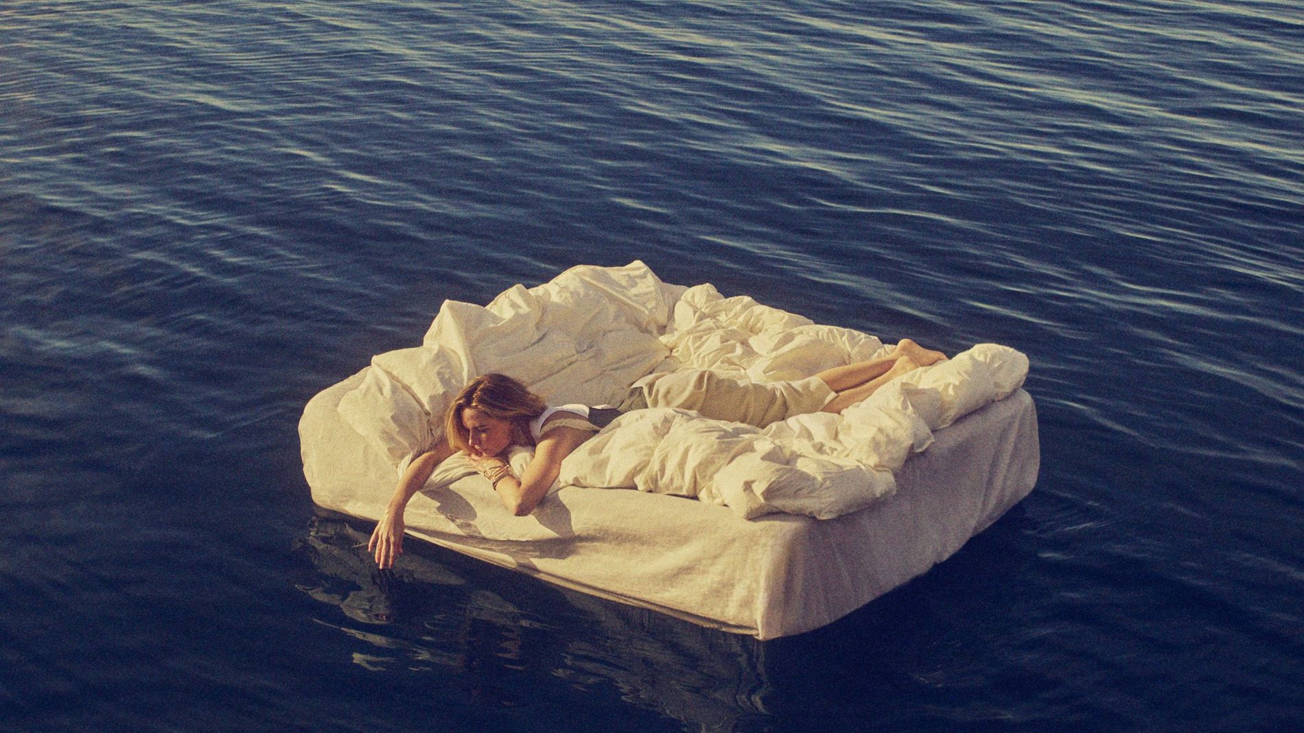 Rebecca Fergusson floats at sea on a mattress. She lies on a white fluffy duvet