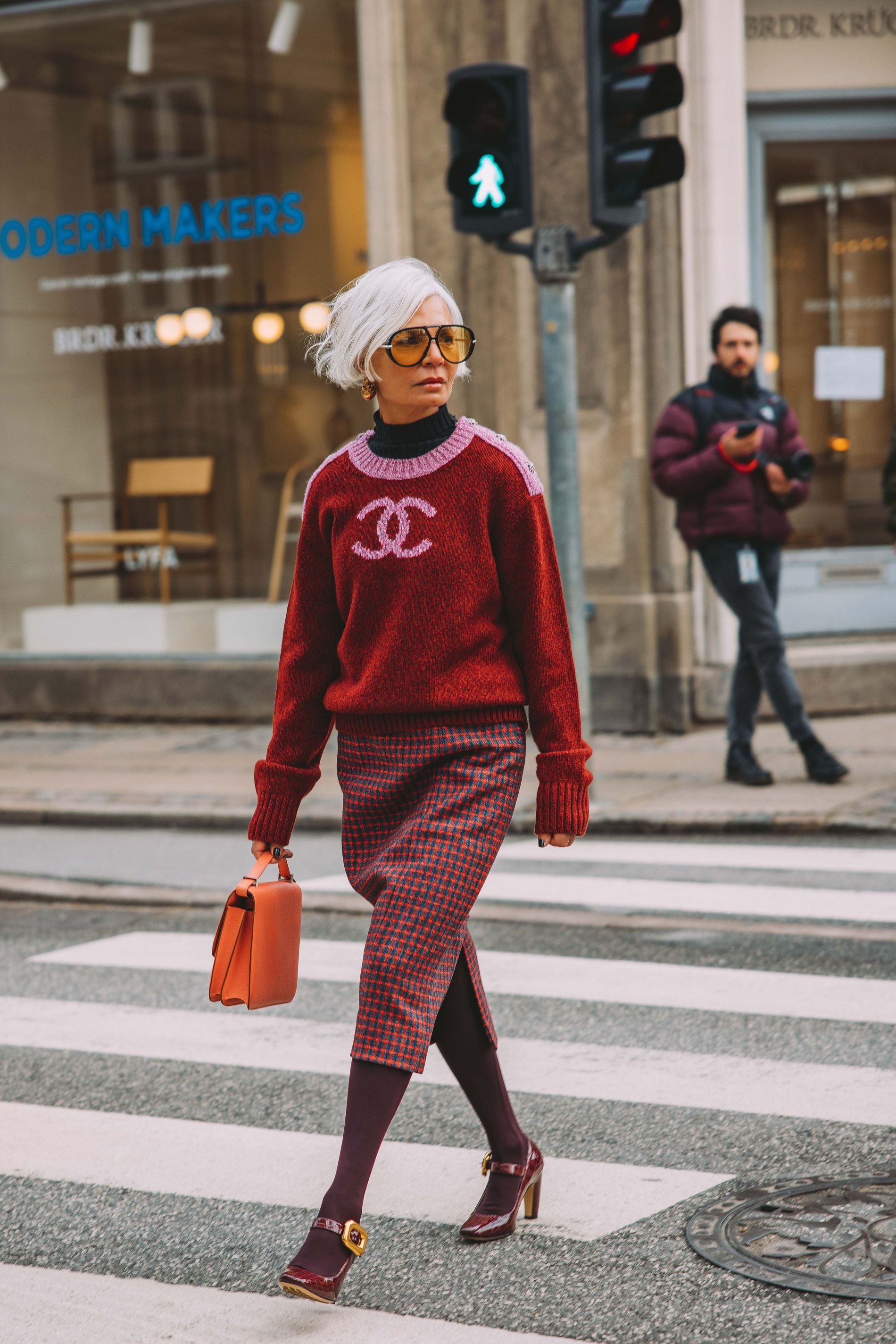 A guest at CPHFW poses for a street style photo wearing a pink and red Chanel sweater and a red checkered skirt