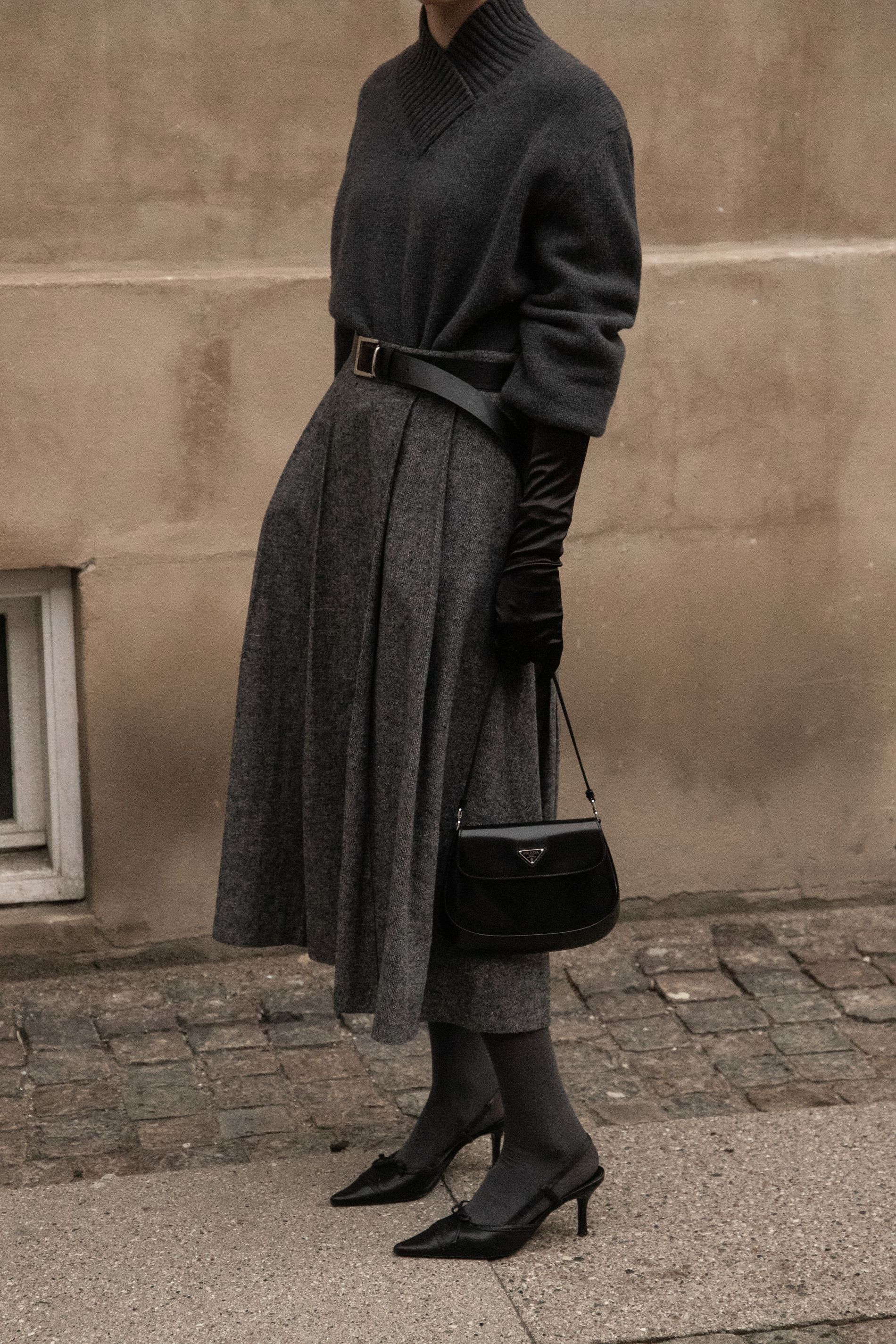 A guest wears a grey knit sweater with pushed up sleeves and tall gloves, paired with a pleated grey wide midi skirt, grey stockings and black kitten heels