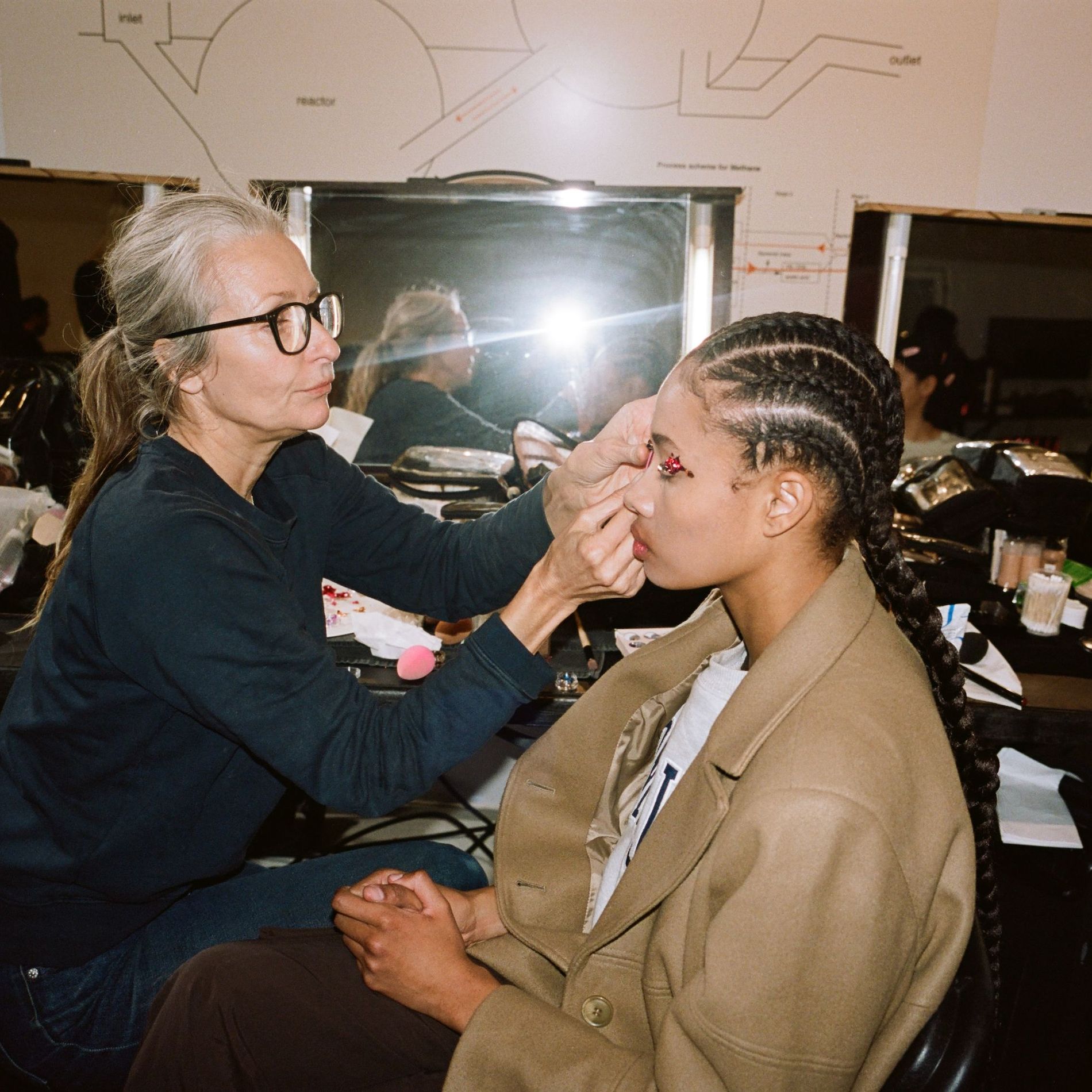 Makeup artist applies sequins to a model's eyes backstage at Ganni's AW23 show