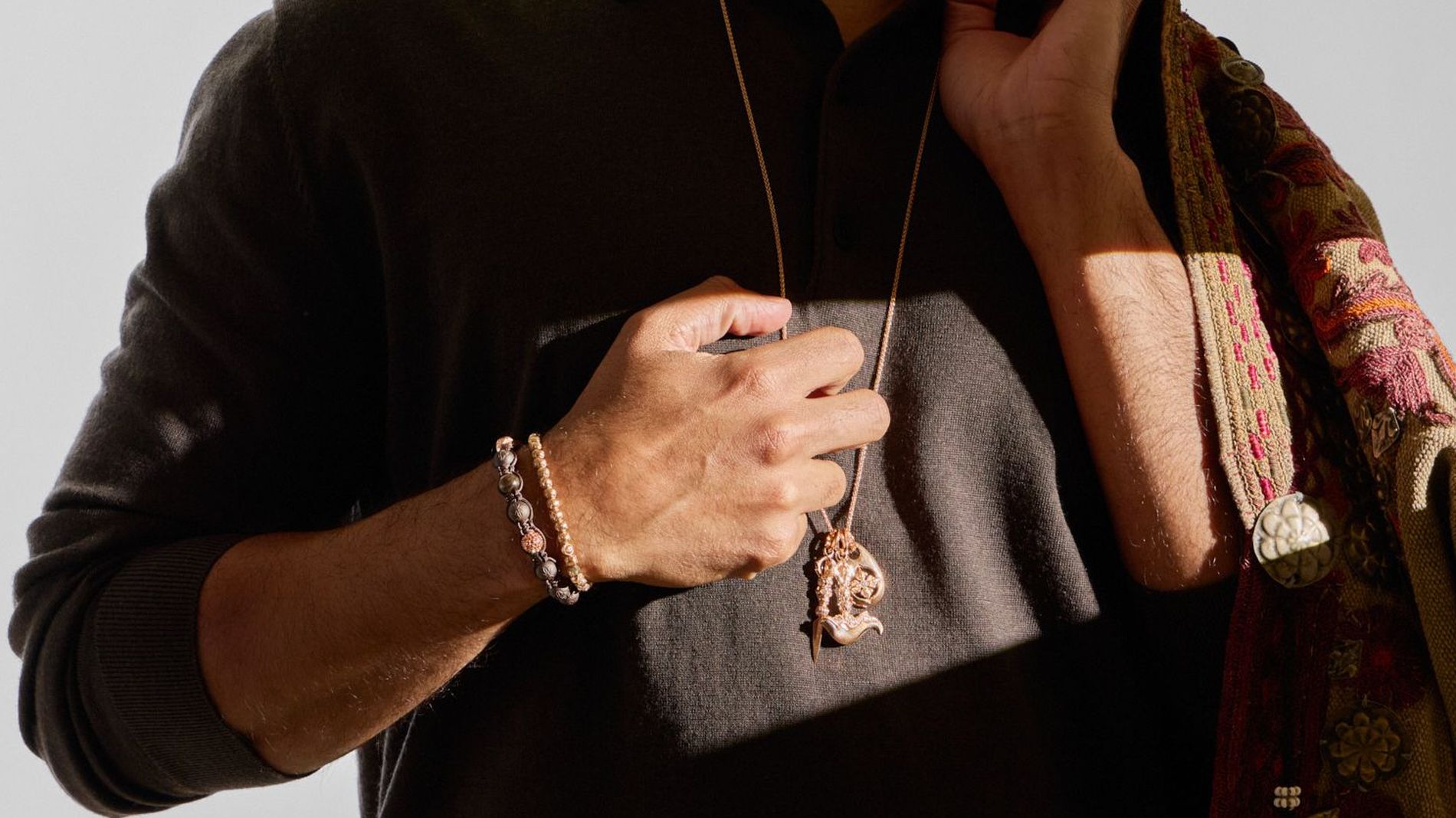 A dark knit polo shirt styled with a long metallic pendant necklace and stacked beaded gemstone bracelets