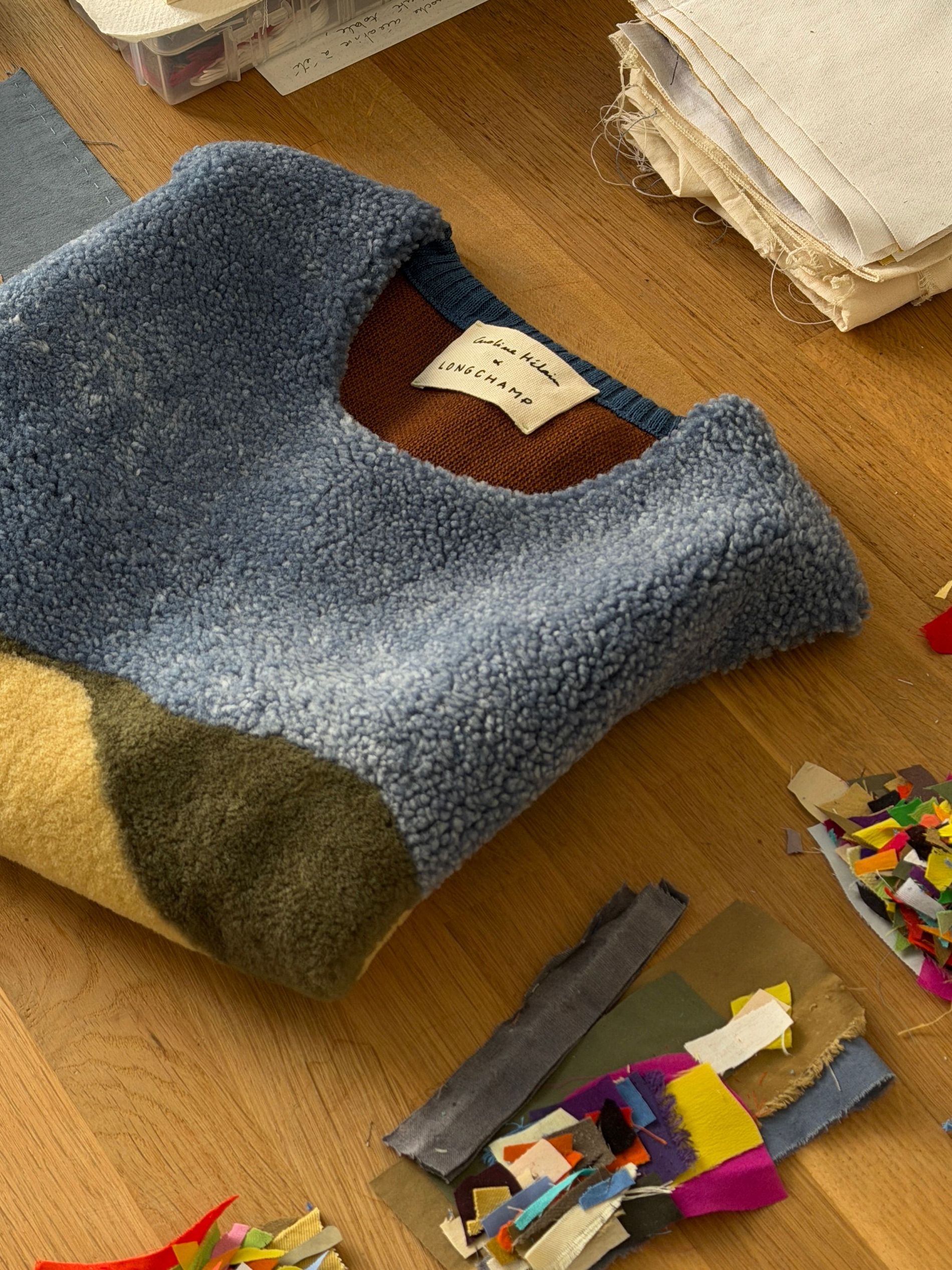 The sleeveless calf leather and bouclé wool top from the Caroline Hélain x Longchamp collection, laid out in Hélain's Brussels studio beside spools of embroidery thread and offcuts from her fabric archive.