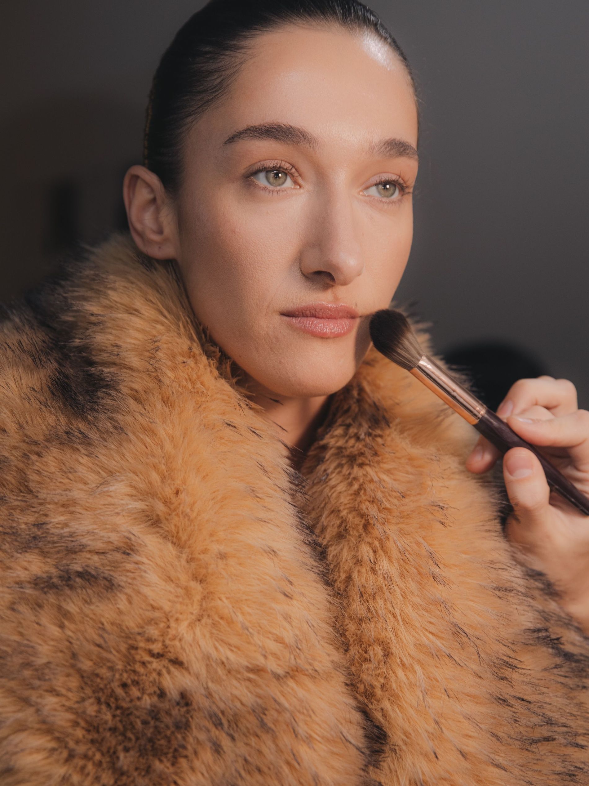 Finishing powder is applied to Bella Tilbury wearing a faux fur coat during final touches in the backstage Rotate AW25 lineup