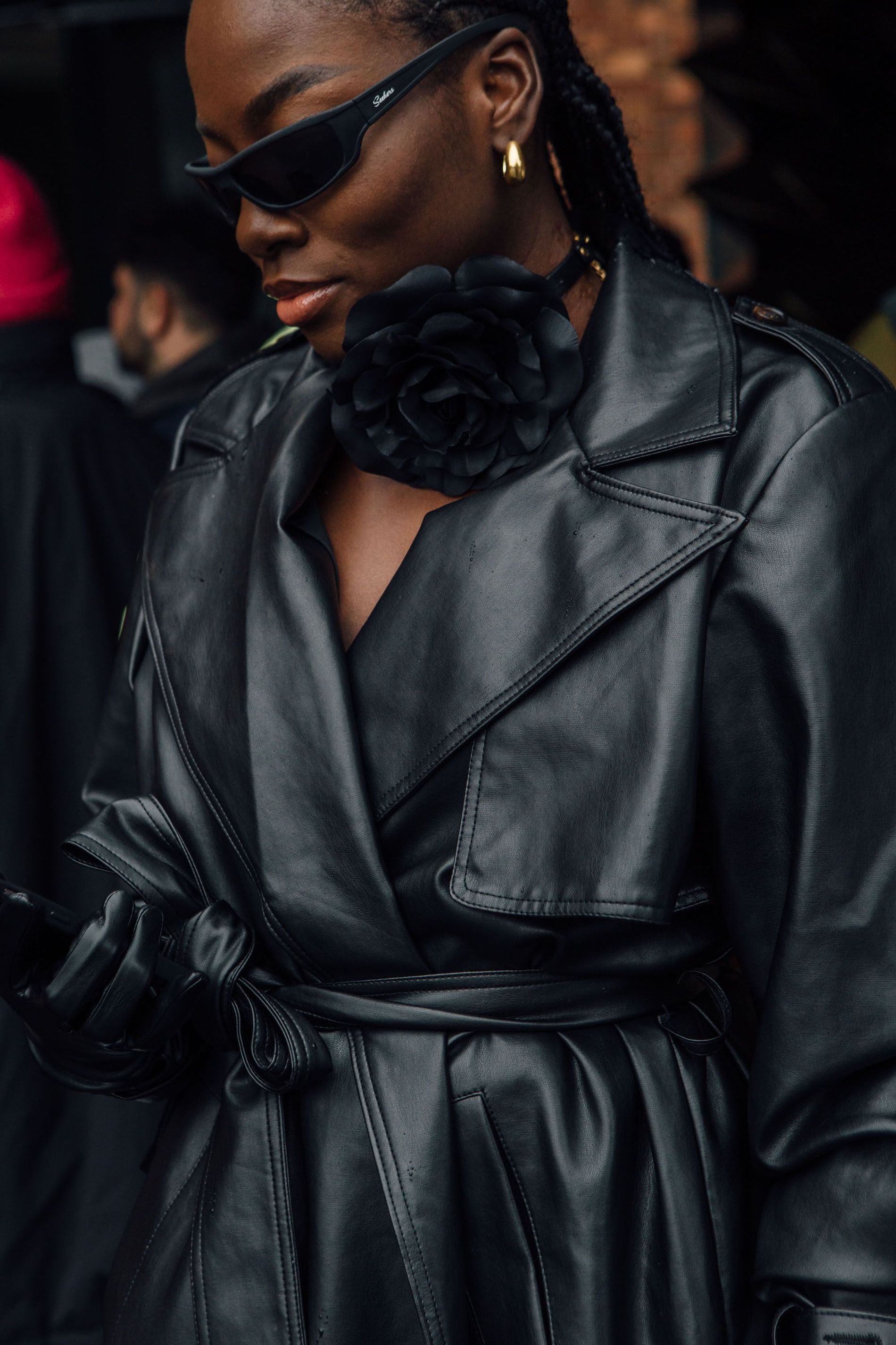 Guest wears a black floral brooch pinned to a chocker and a black leather trench