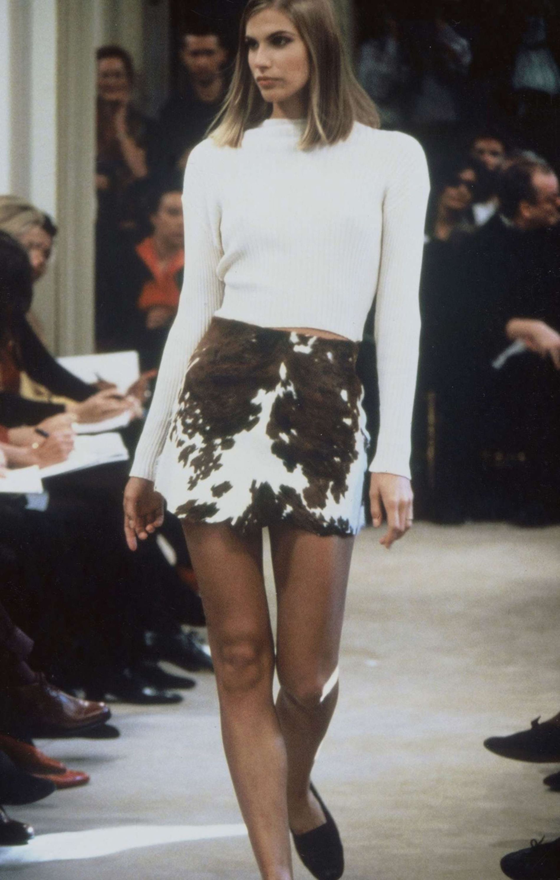 Model wearing a cropped cream knit and brown cow print mini skirt, styled with black ballet flats in a ’90s-inspired look