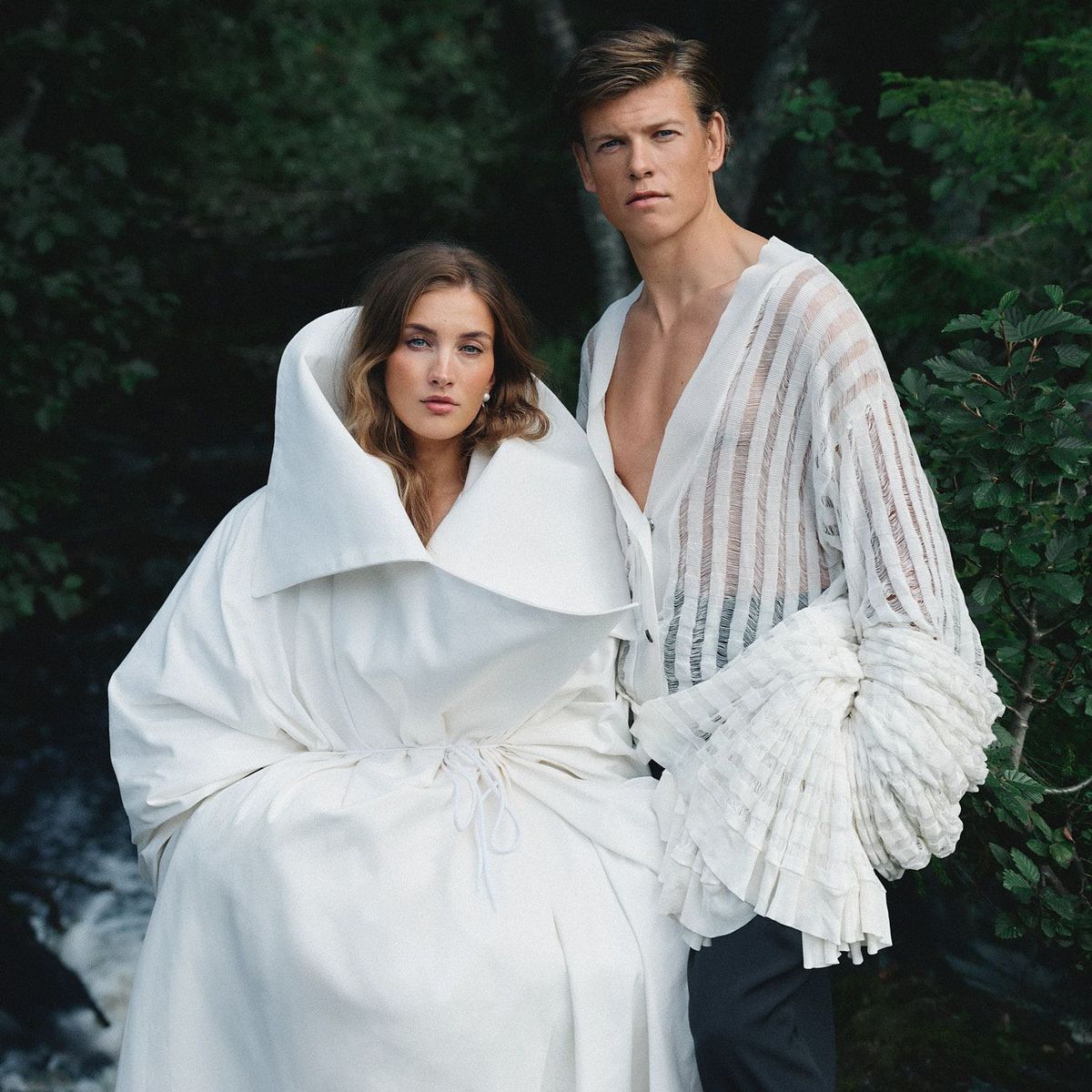 Klæbo and Døsvik stand against a forrest and river background wearing all white from Caucasian brand Institution