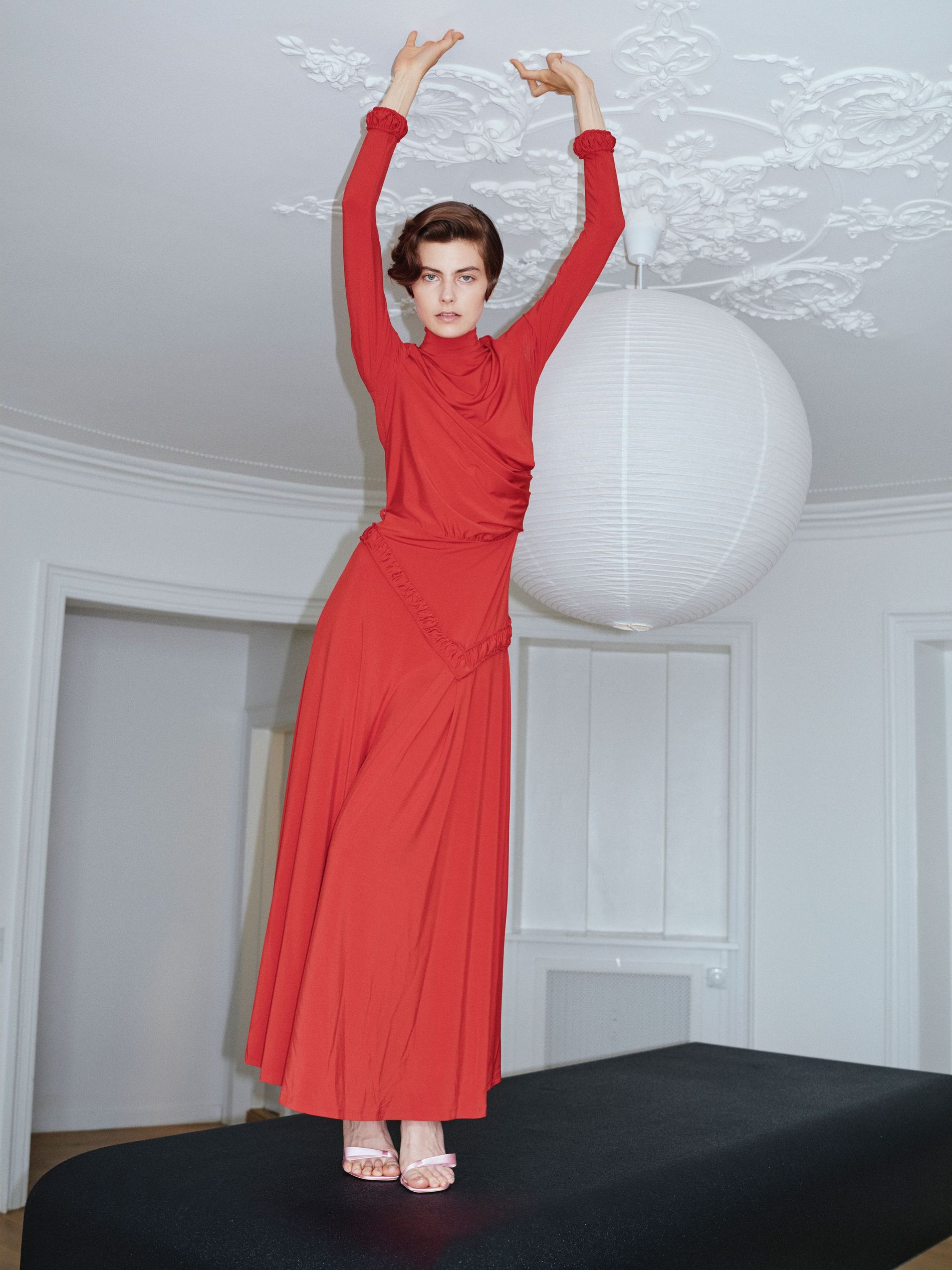 Image from Forza Collective SS27, model in a red dress standing on a table.