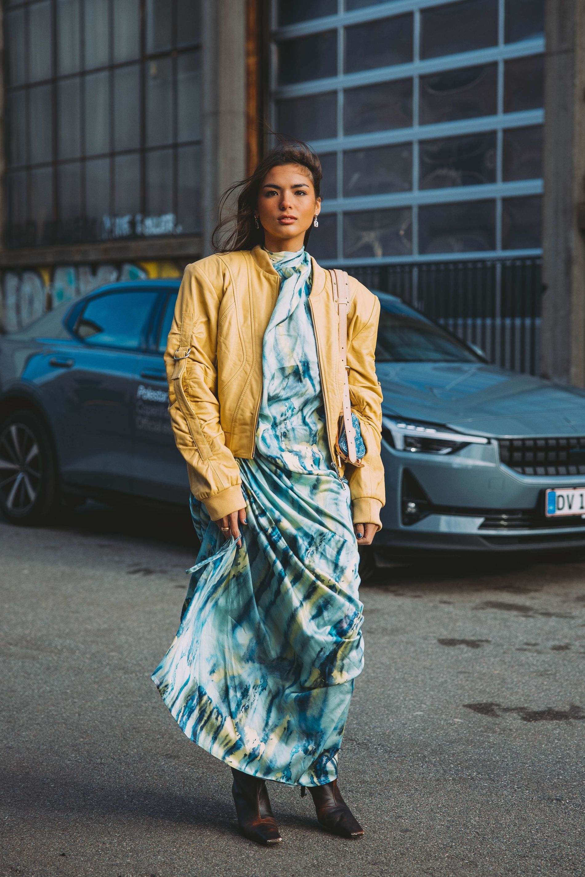 A guest wears a butter yellow bomber jacket paired with a tie dye blue dress and brown boots