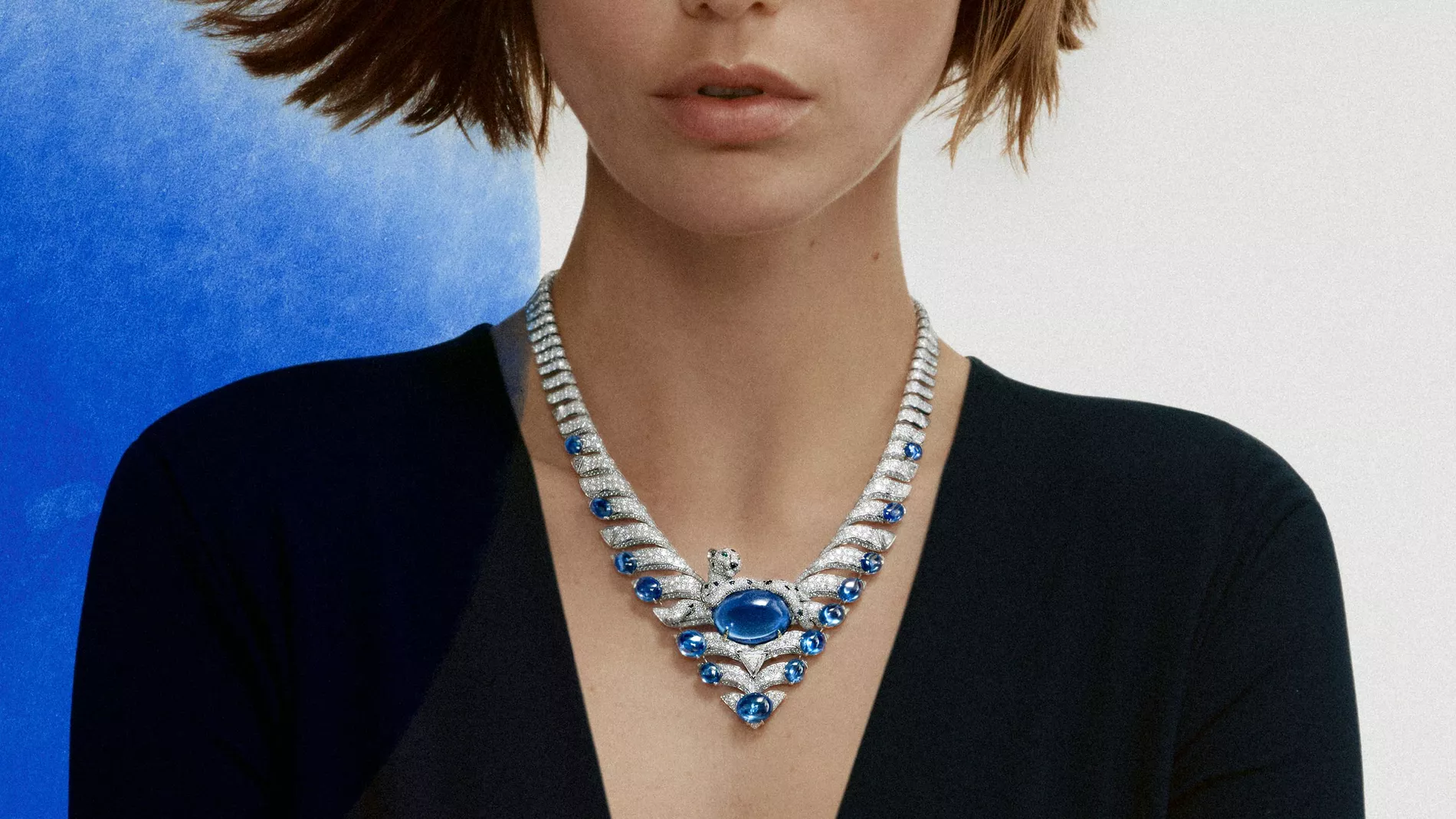 Model in black wears a necklace from Cartier high jewellery against a white background with a blue swipe of paint