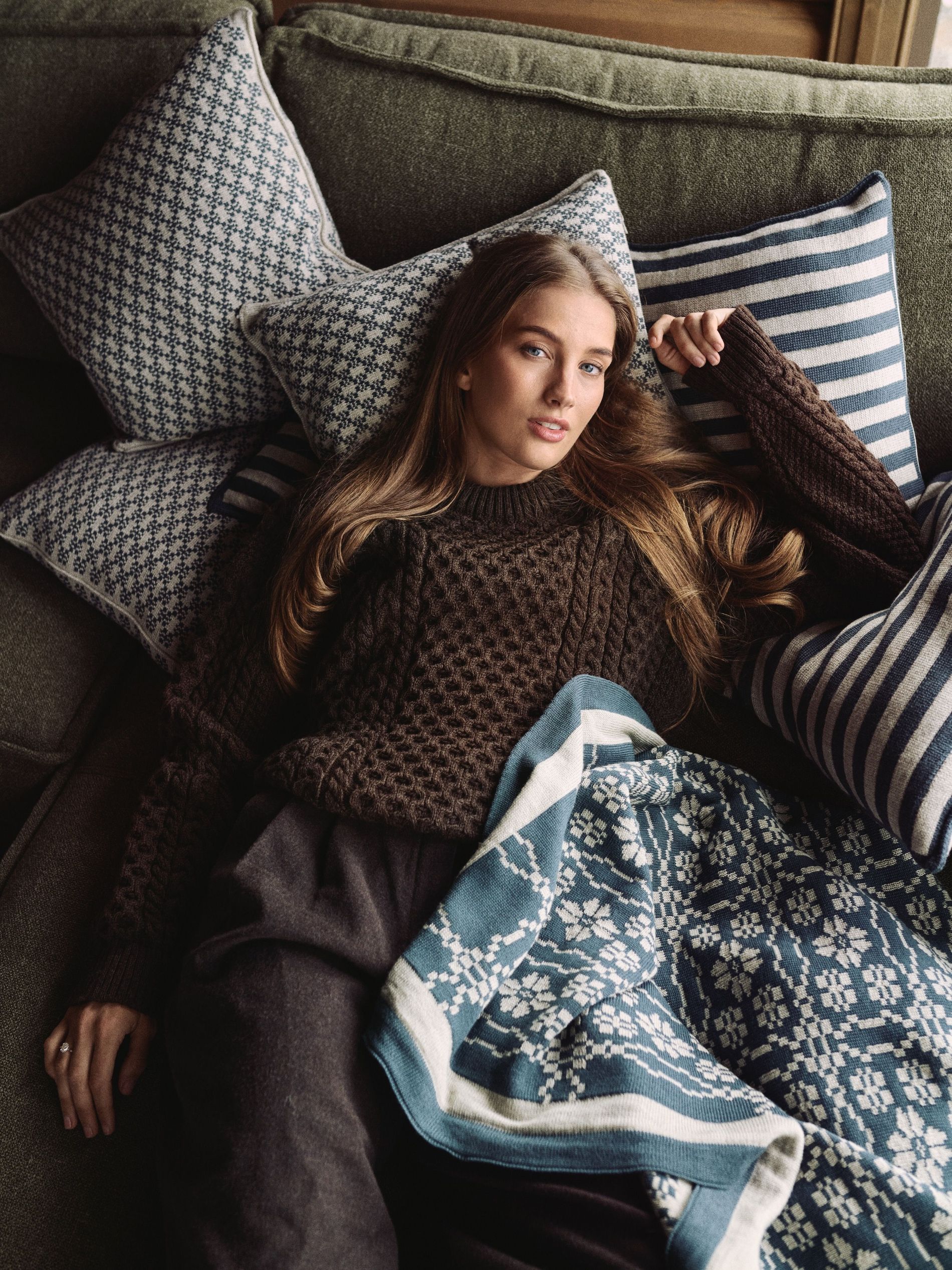 Pernille Dosvik lounges in a Dale of Norway sweater on the sofa with pillows and a blanket from her Dale of Norway collaboration