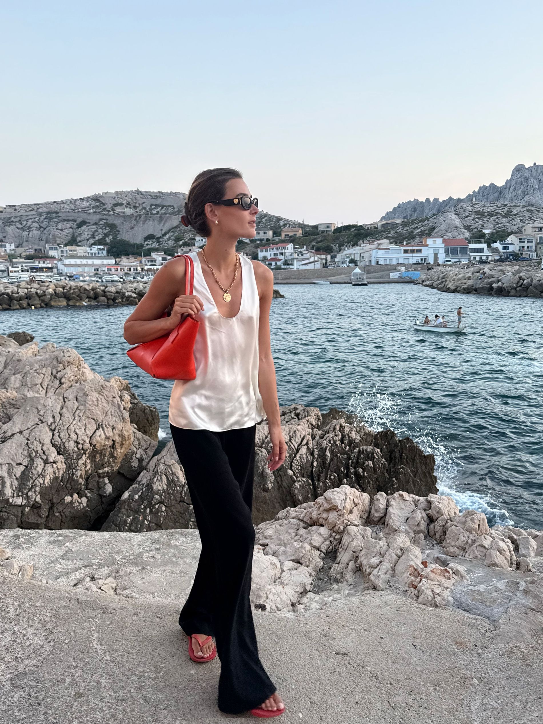 Vera wears red sandals, black trousers, white satin top and red handbag