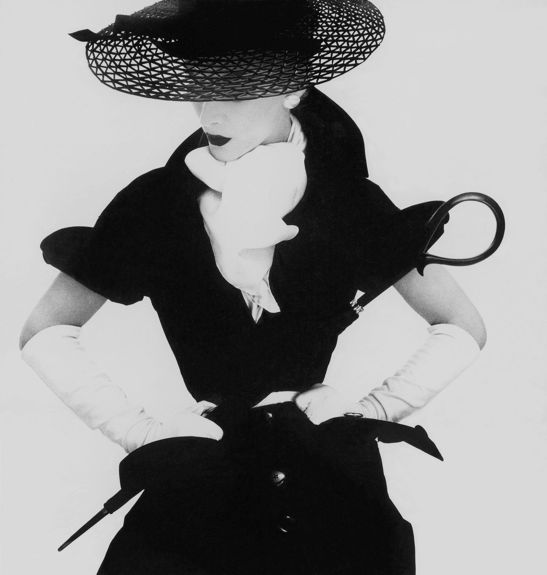 Model Lisa Fonssagrives-Penn wearing a black dress with a white scarf, gloves, wide-brimmed hat, and belt, holding umbrella