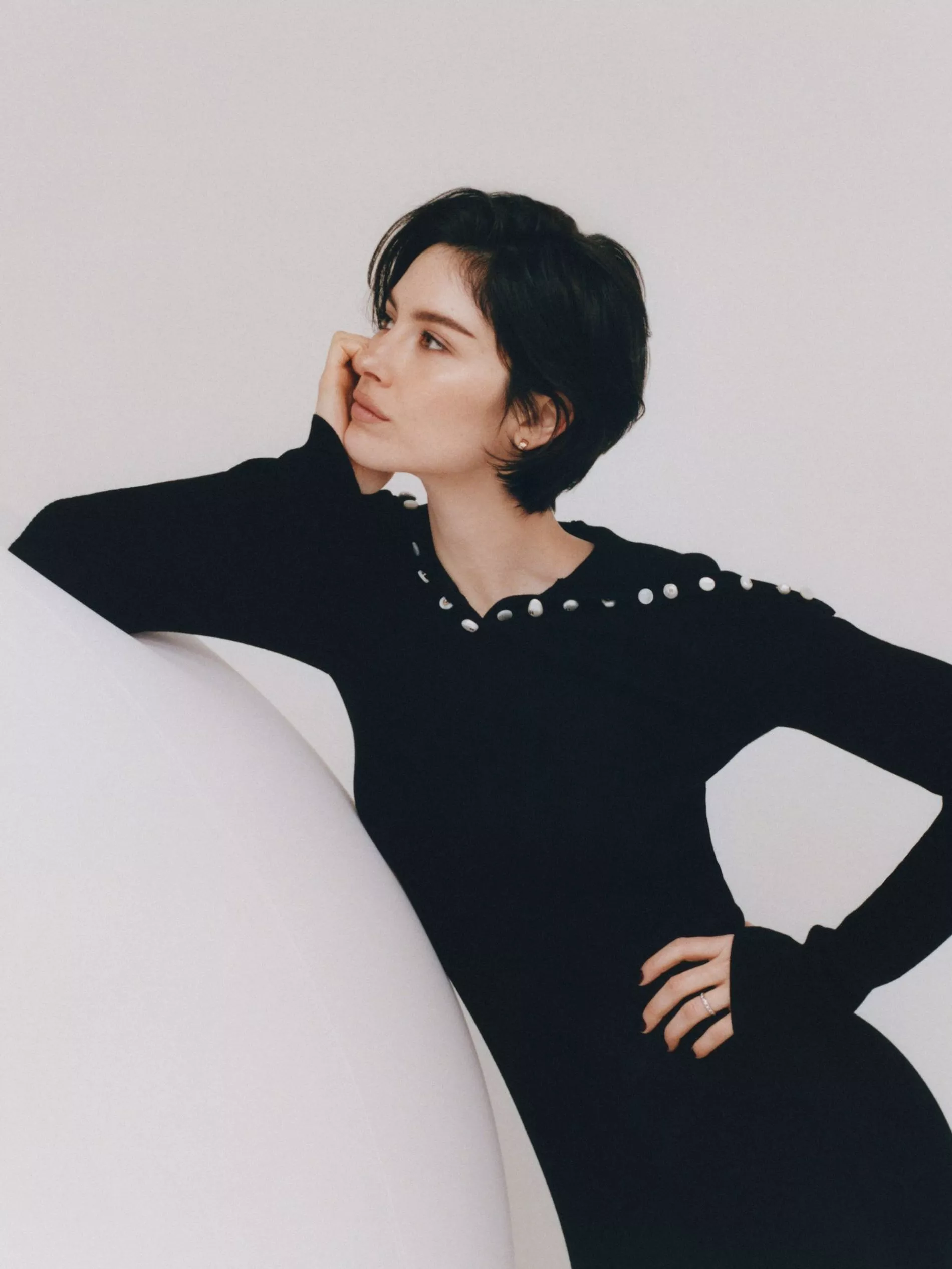Gracie Abrams poses in a black knitted dress on a white soundstage for the Coco Mademoiselle Cursh Absolu campaign