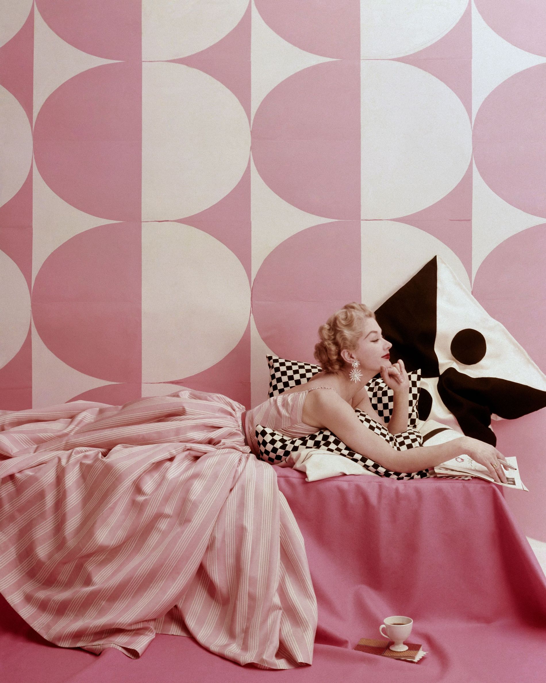 Model Lisa Fonssagrives lounging on bed, wearing Claire McCardell's pink and white striped dress