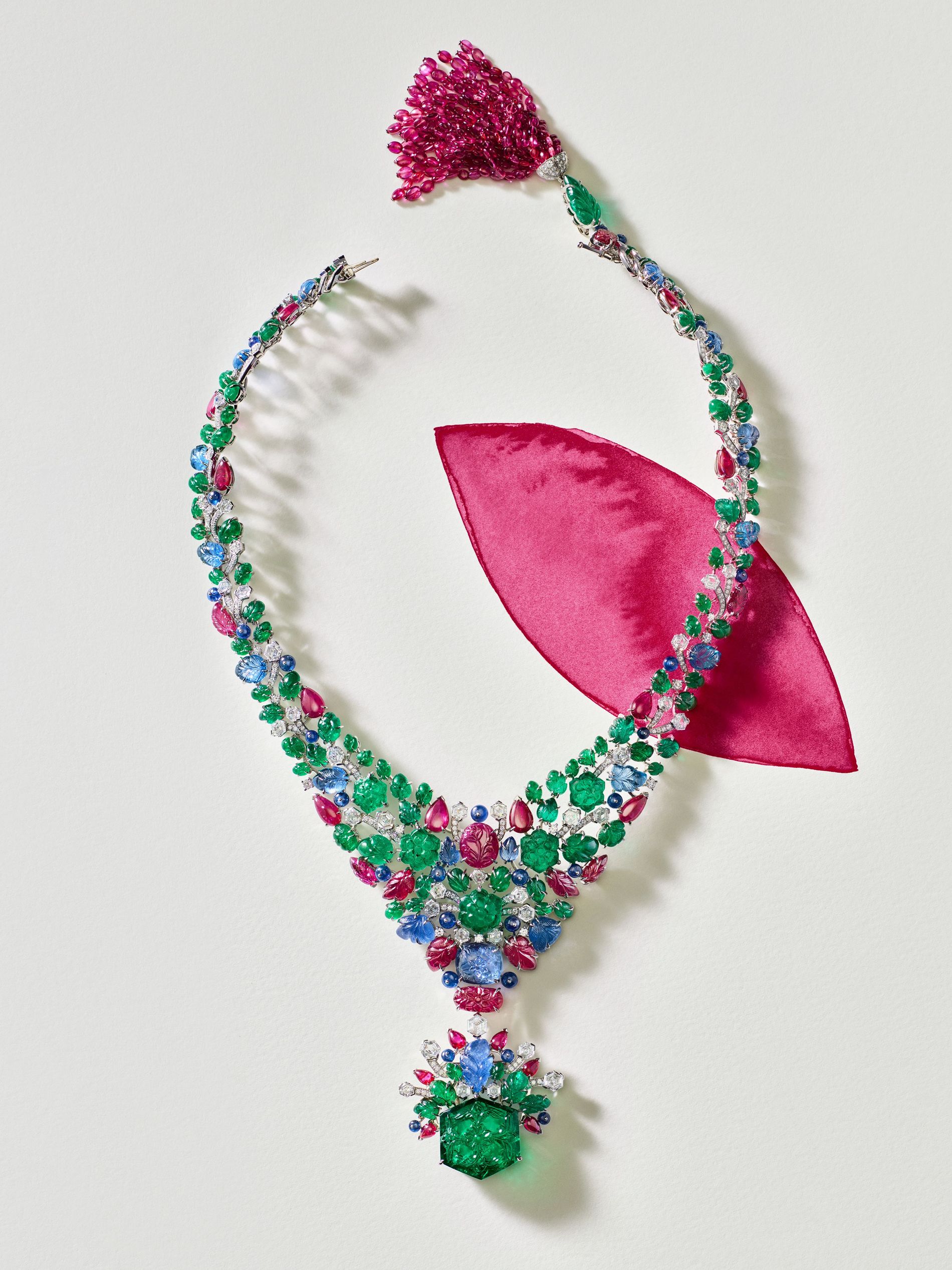 a multi coloured gemstone necklace from Cartier high jewellery againsyt a white background with a pink petal painted 