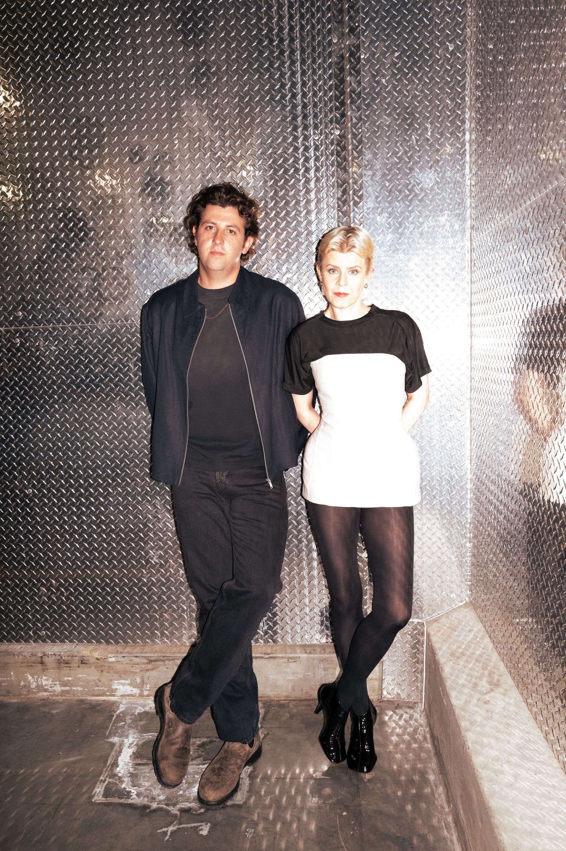 Jamie XX and Robyn leaning against an aluminium wall