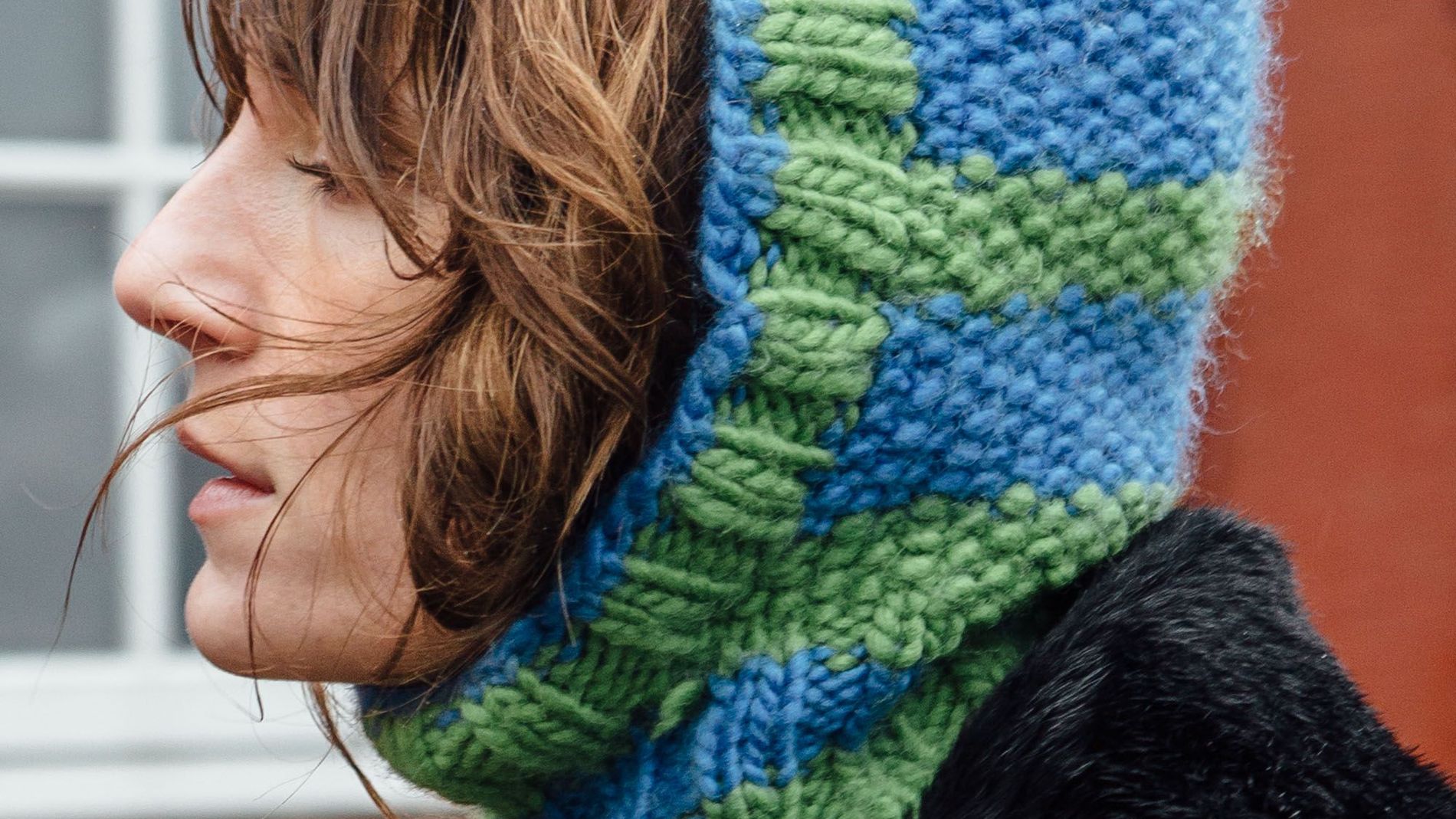 A street style CPHFW AW23 guest wears a green and blue patterned balaclava, and pin-striped coat with a faux fur collar