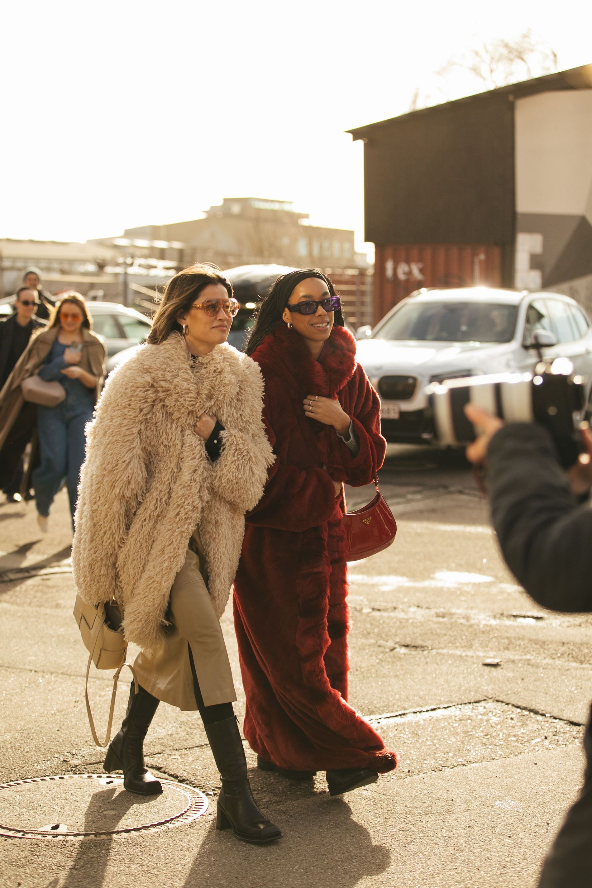 Two guests at CPHFW poses for a street style photo wearing monochromatic red and beige looks featuring fur coats