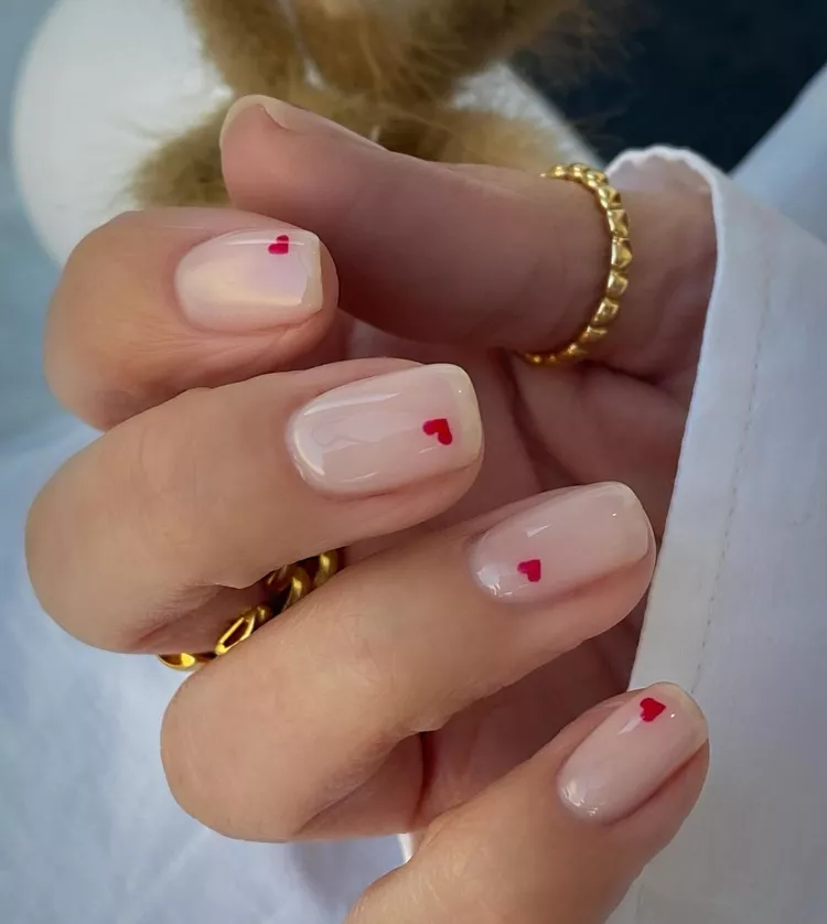 Small red hearts are painted onto a neutral base, creating a minimalist square manicure for Valentine's Day