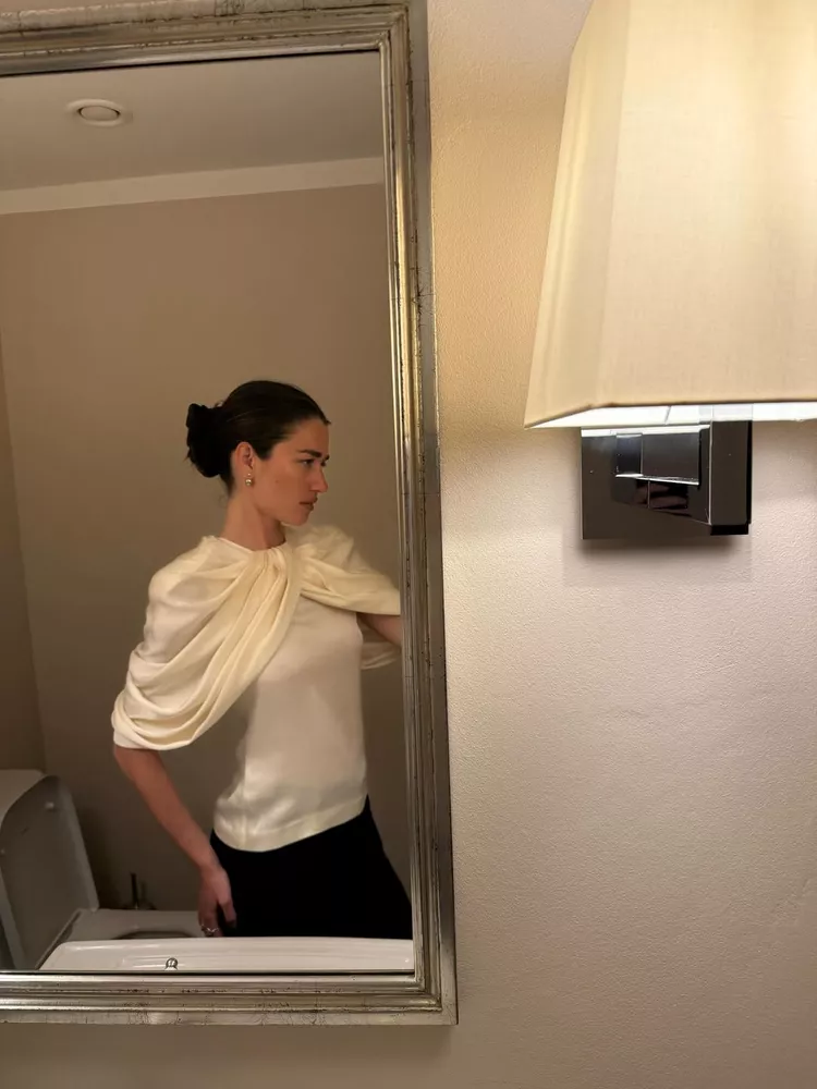 Ilirida Krasniqi wear a draped white silk top and black trousers posting in a mirror selfie