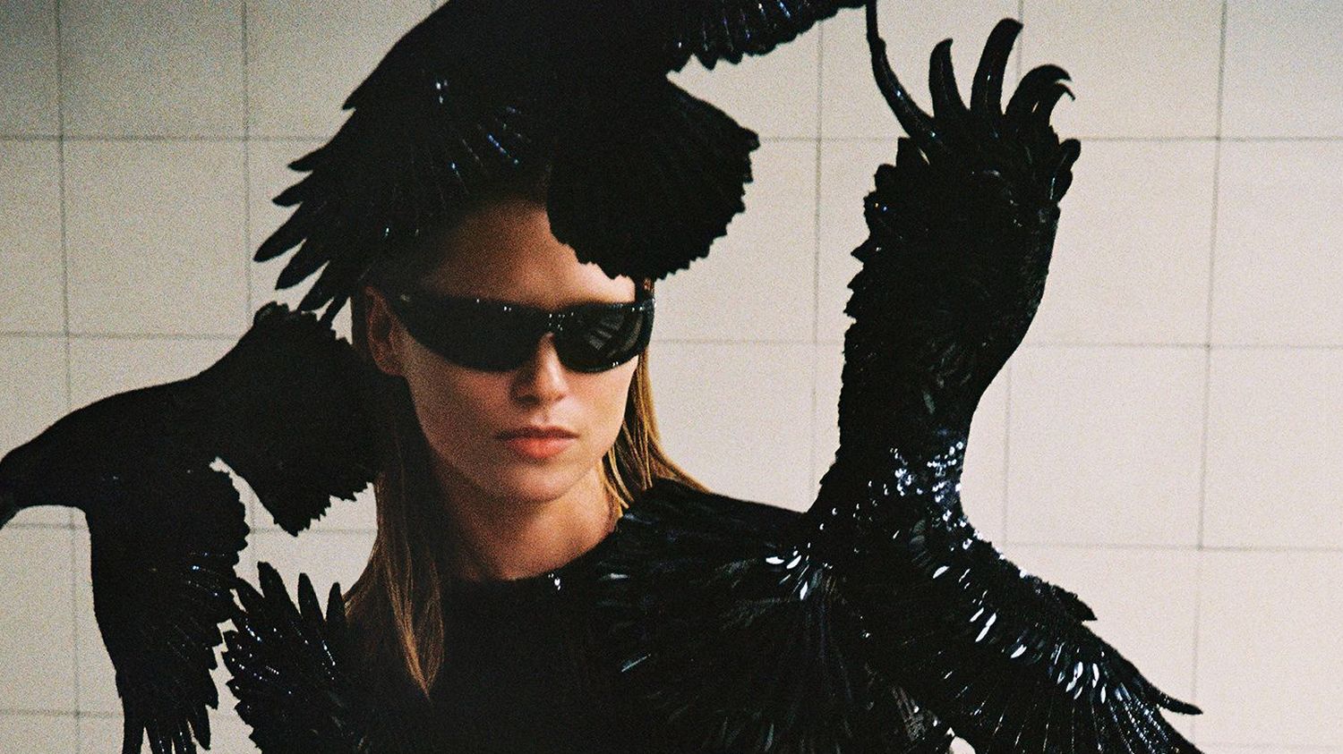 Model in black catsuit with crows in a white tiled room