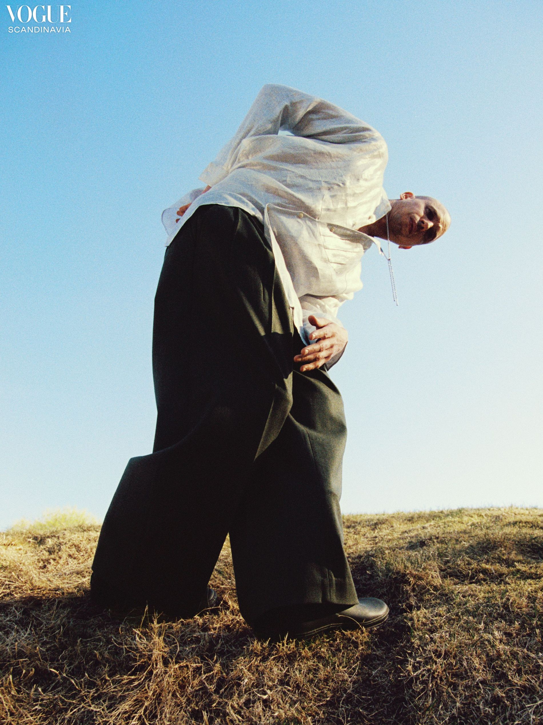 Model is staning in the nature wearing a metalic silver linen shirt and green wool trousers