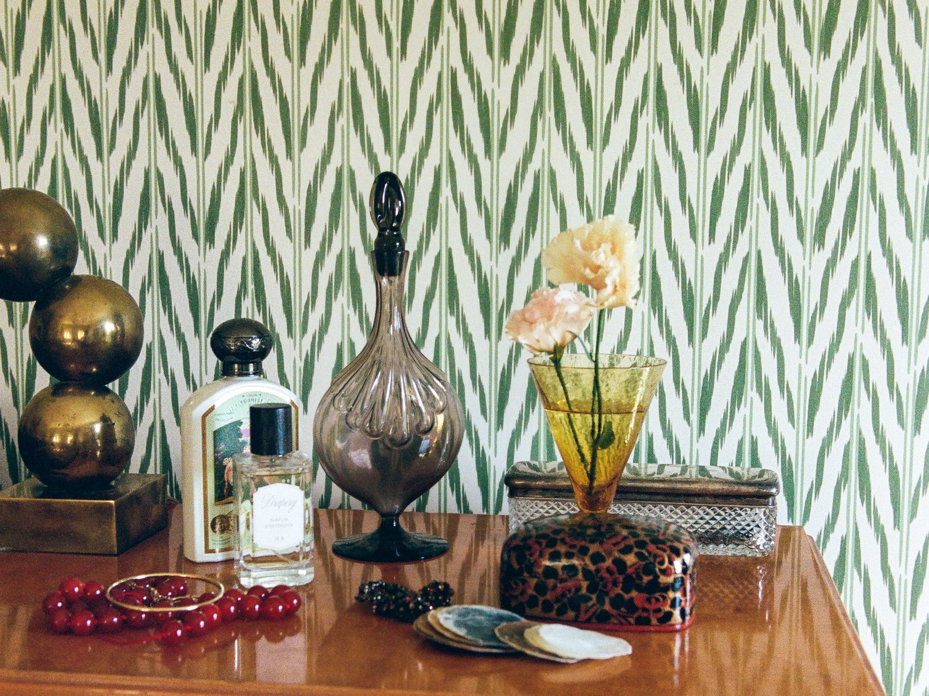 A close up of a table with trinkets behind which is Helene Blanche's Painted Ikat Wallpaper in Green Earth