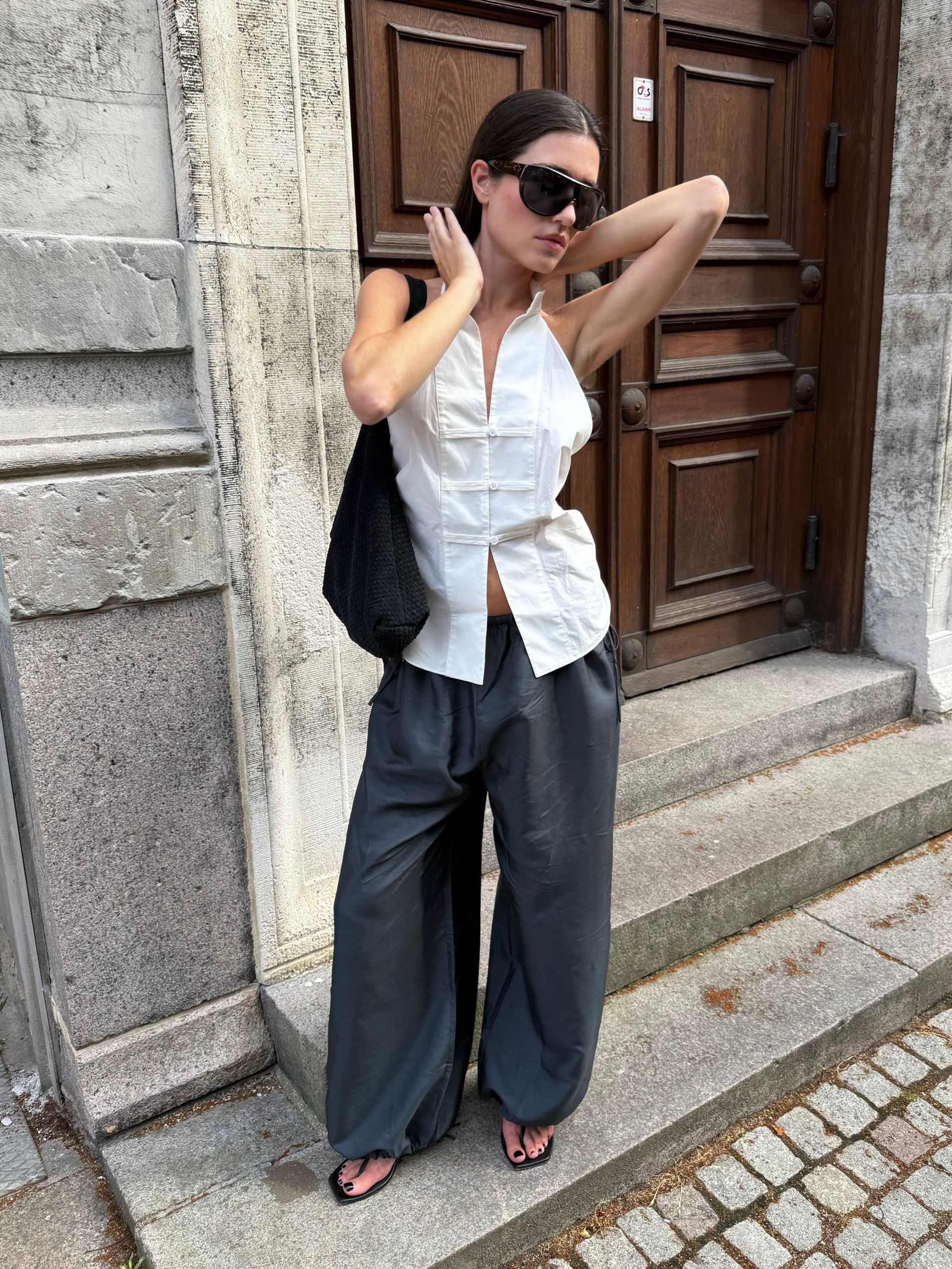 Ilirida Krasniqui at CPHFW SS27 wearing St Agni white top, grey trousers, flip flops, sunglasses and tote bag