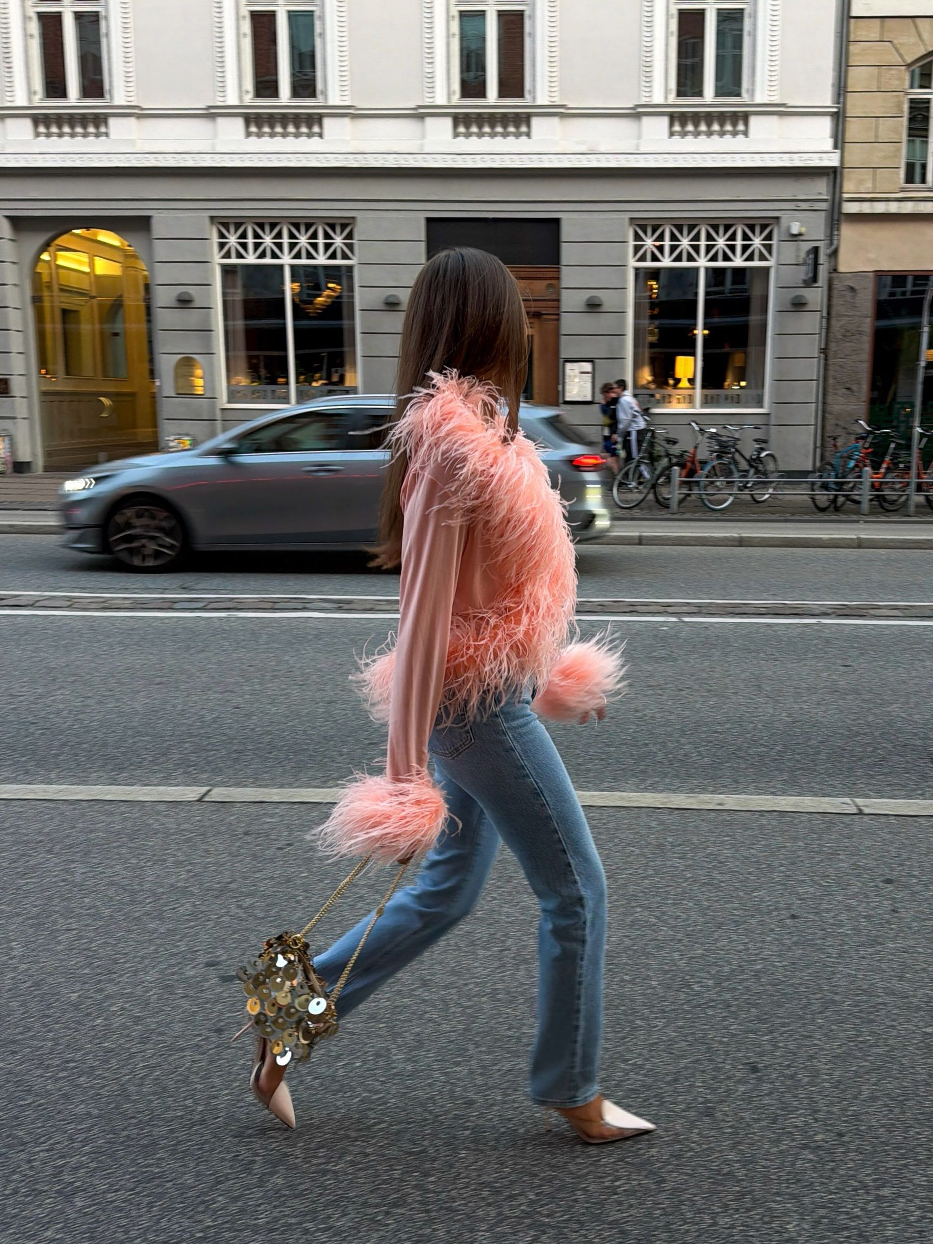 Nina Sandbech wears a pink feathered top, light wash jeans, beige heels and sequined bag to CPHFW 