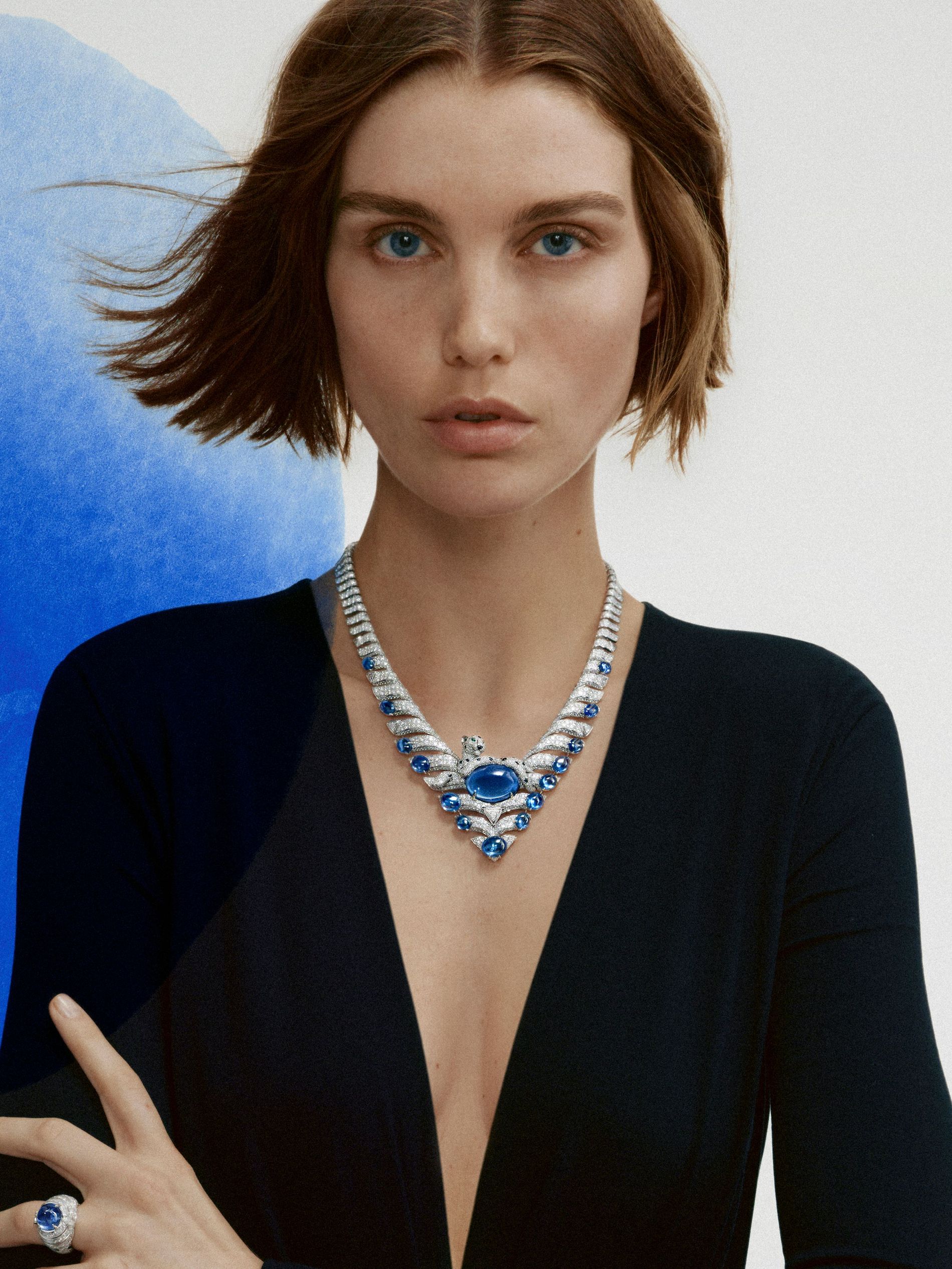 Model in black wears a necklace from Cartier high jewellery against a white background with a blue swipe of paint