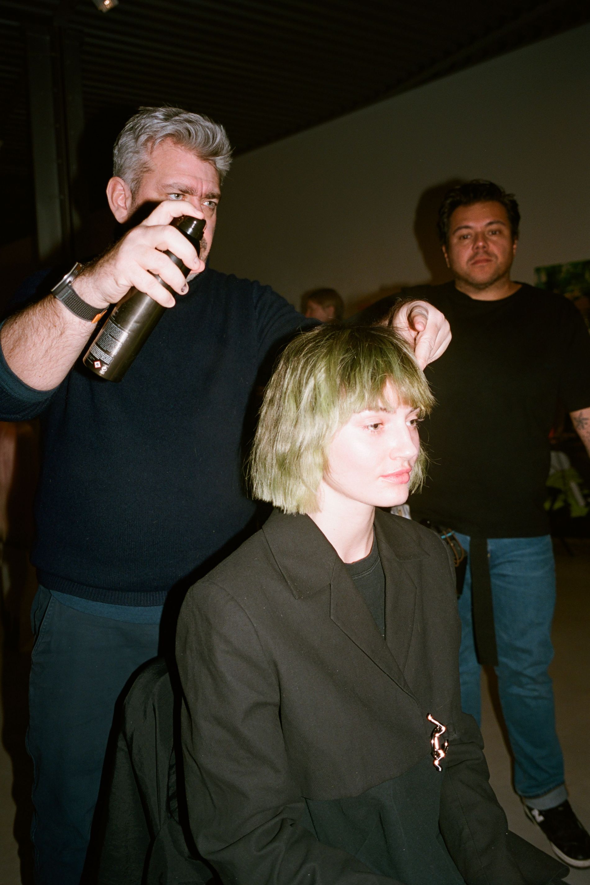 Cim Mahony adjusts a model wearing a green bob with fringe backstage at Ganni's AW23 fashion show