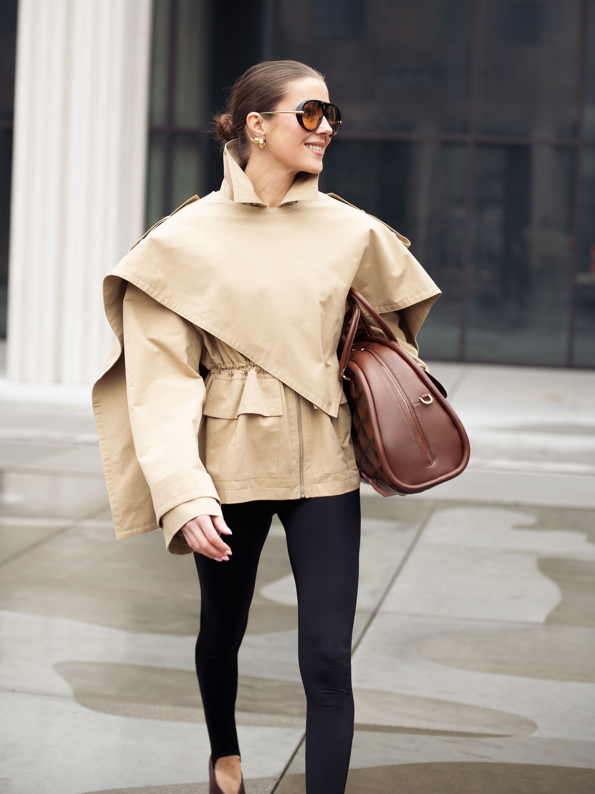Nina Sandbech wears her hair slicked back into a bun, paired with sunglasses, a trenchcoat and a brown bag