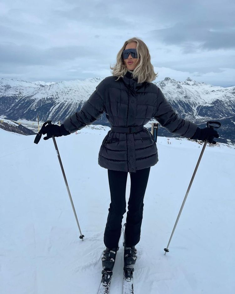 Elsa Hosk poses in a cinched black ski jacket and skinny ski trousers and black shield glasses