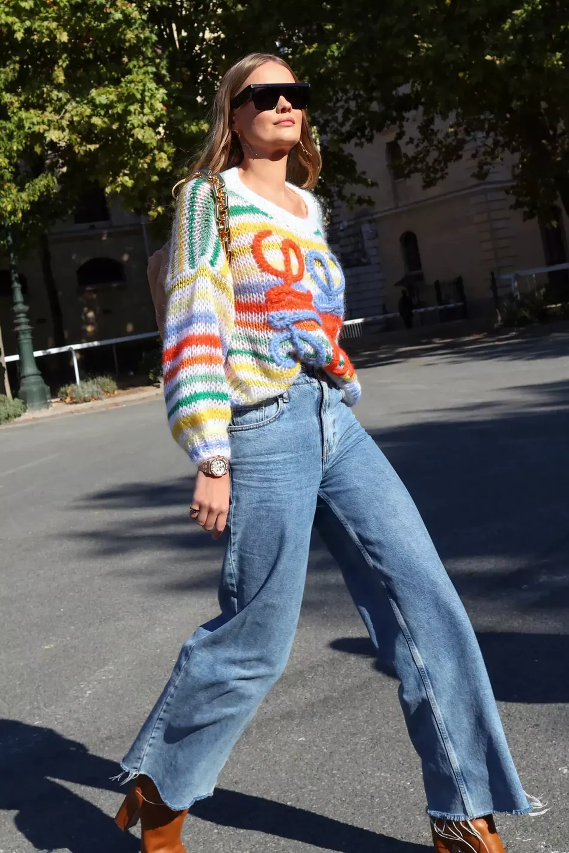 Paris fashion week guest wears colourful striped sweater with blue jeans and heeled brown boots 