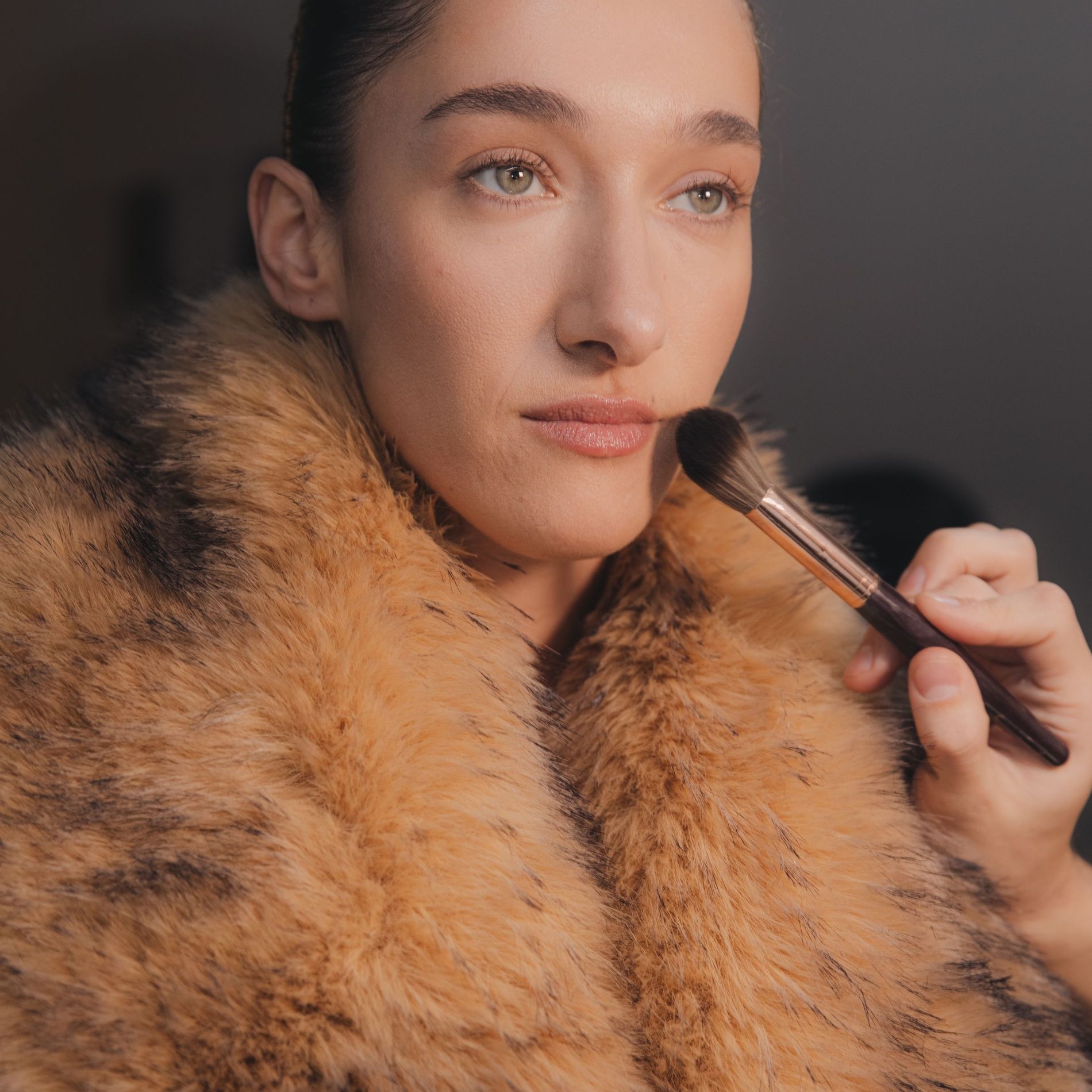 Finishing powder is applied to Bella Tilbury wearing a faux fur coat during final touches in the backstage Rotate AW25 lineup
