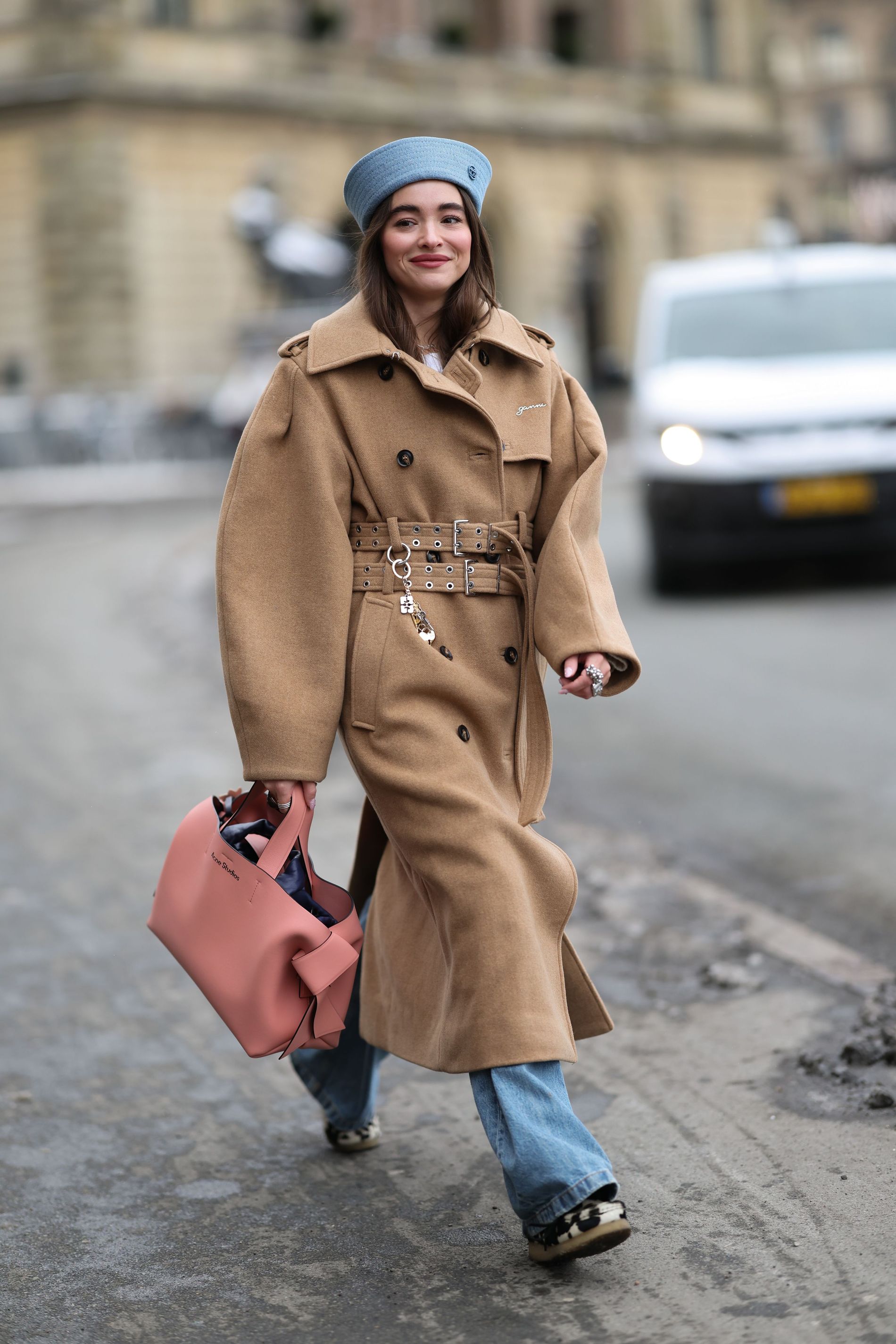 Street style images of Evi Wave wearing a beige oversized trench coat, together with a pink acne studio bag, and blu denim jeans and hat 