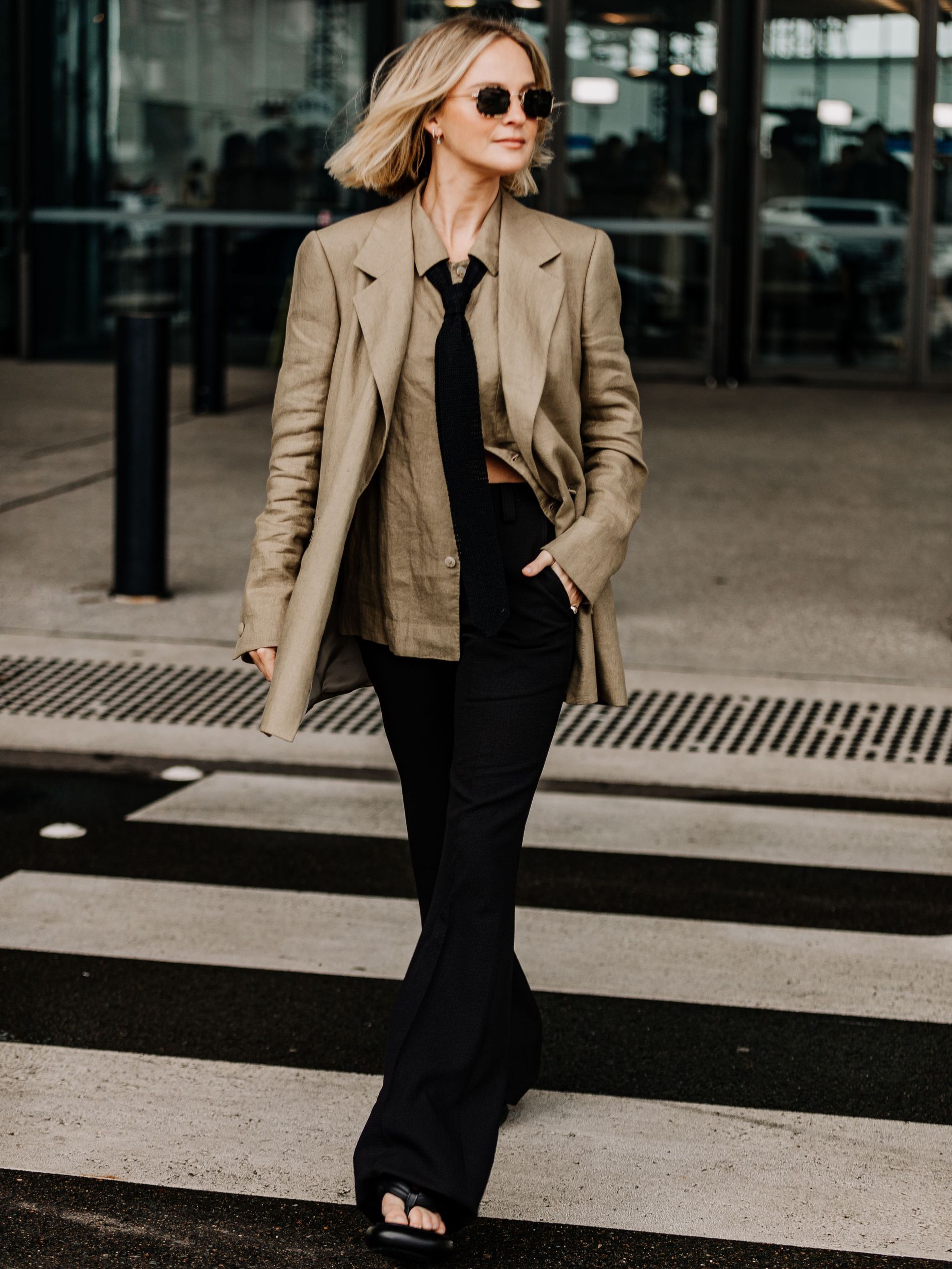 Woman wearing beige blazer and shirt with black necktie and trousers