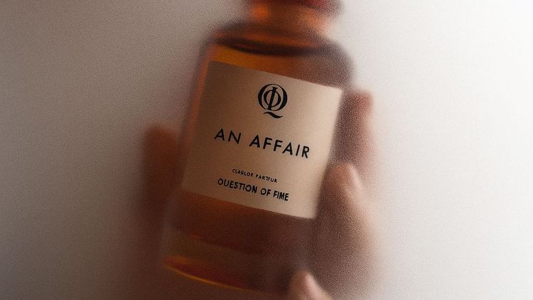 QOT's perfume 'An Affair' held in hand and surrounded by steam