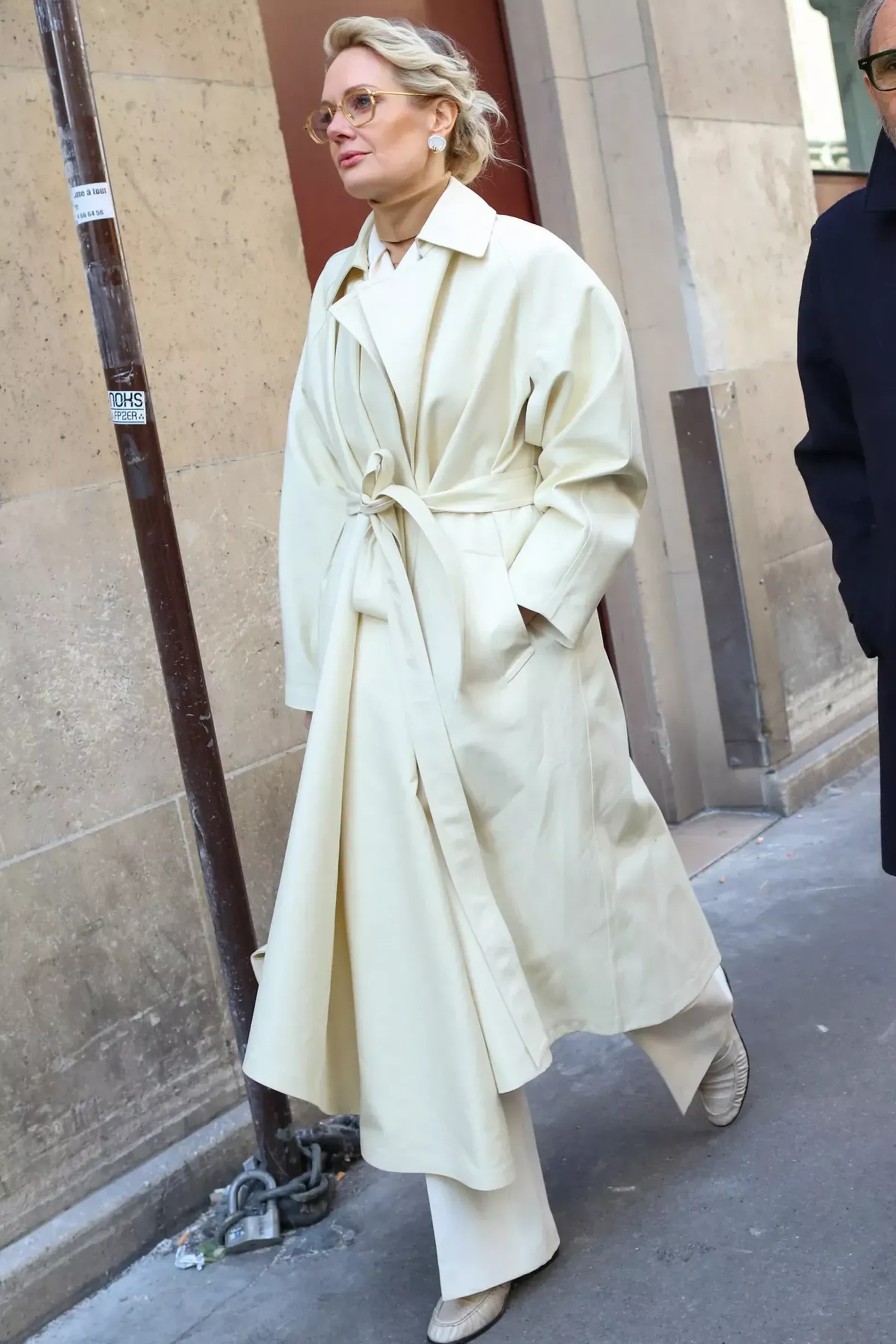 Paris Fashion Week guest wears cream coat over brown turtle neck and suit pants 