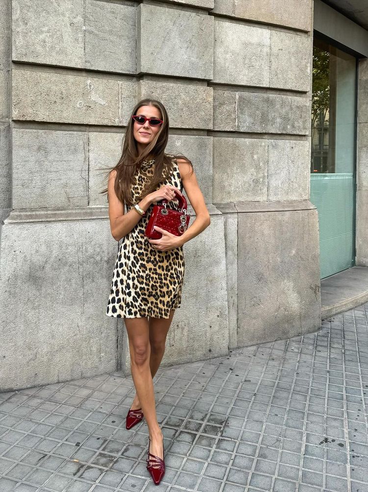 Nina Sandbech wears a leopard print mini dress with burgundy-rimmed sunglasses, a matching red Lady Dior handbag and red pumps