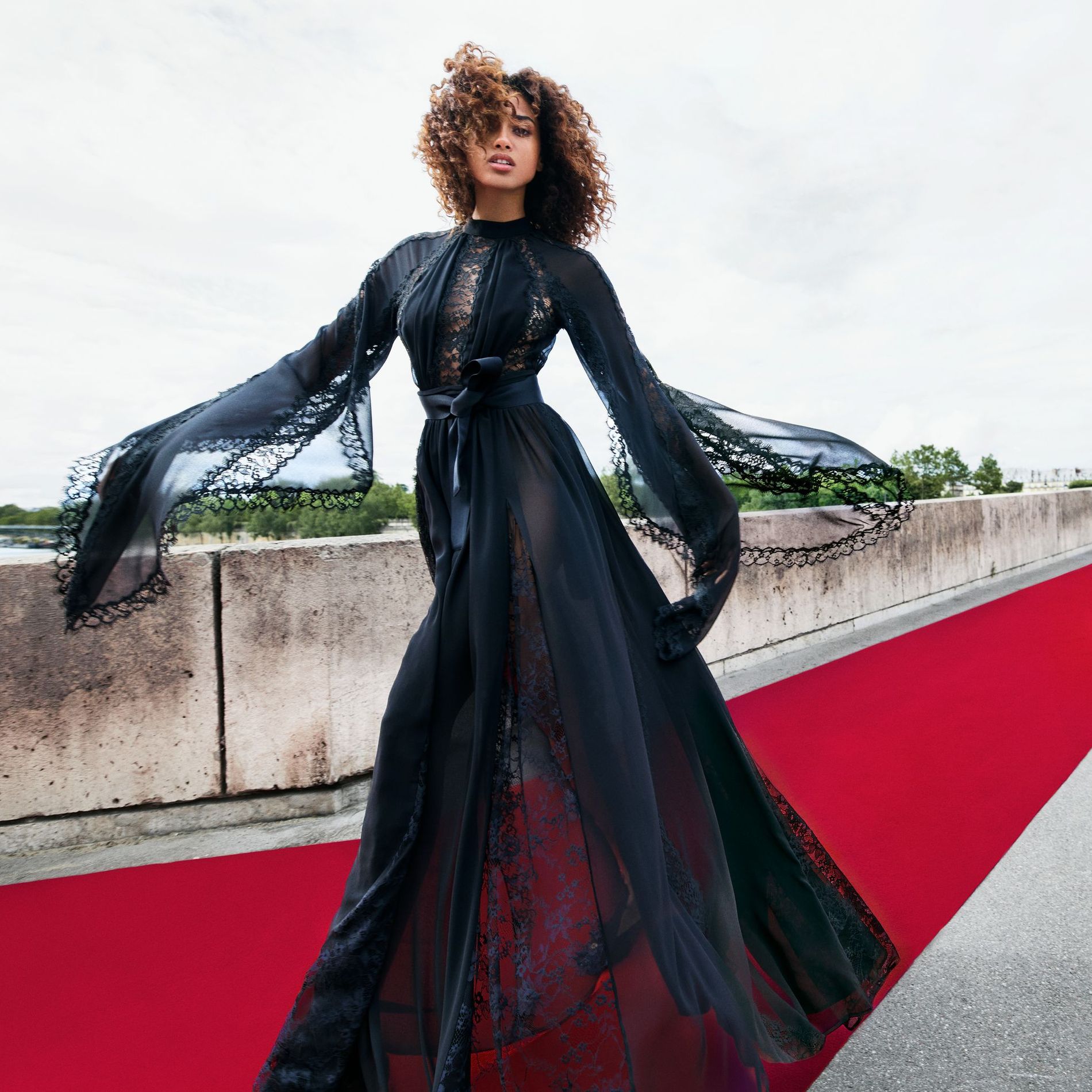 Model walks a red carpet wearing a lace-detailed black formal dress from Elie Saab's new design collaboration with H&M in Paris