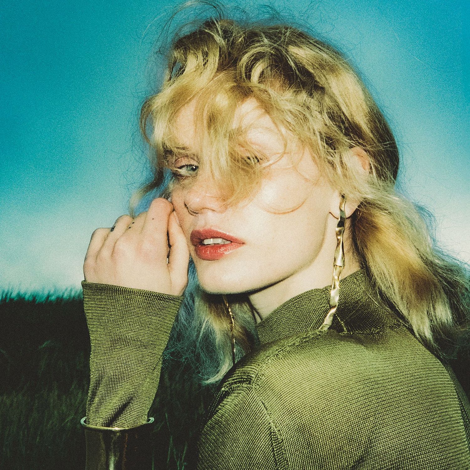 Model with tousled blonde hair and glowing skin looks at the camera framed by the setting summer sun