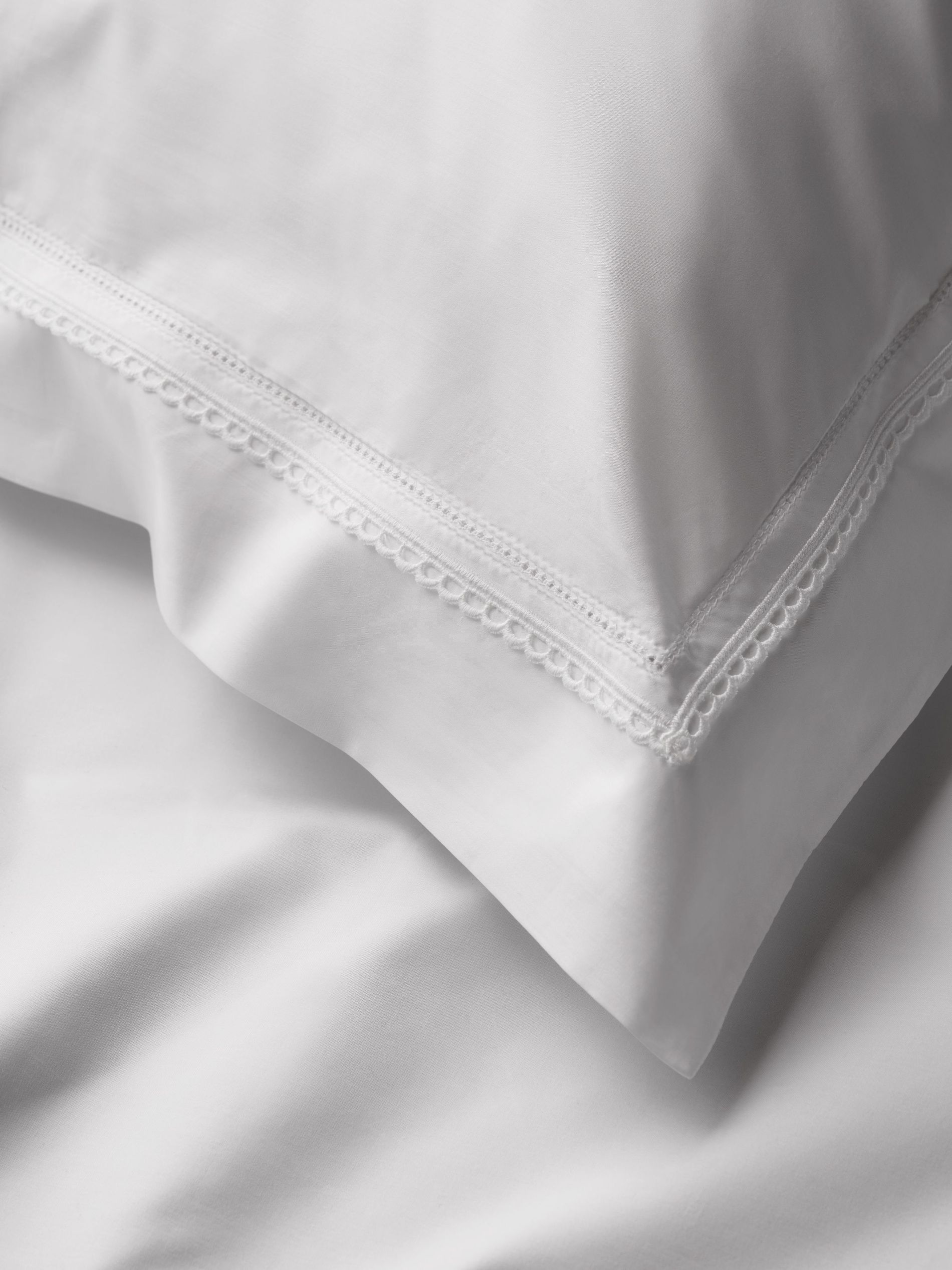 A closeup of white pillowcase with embroidery by Benon