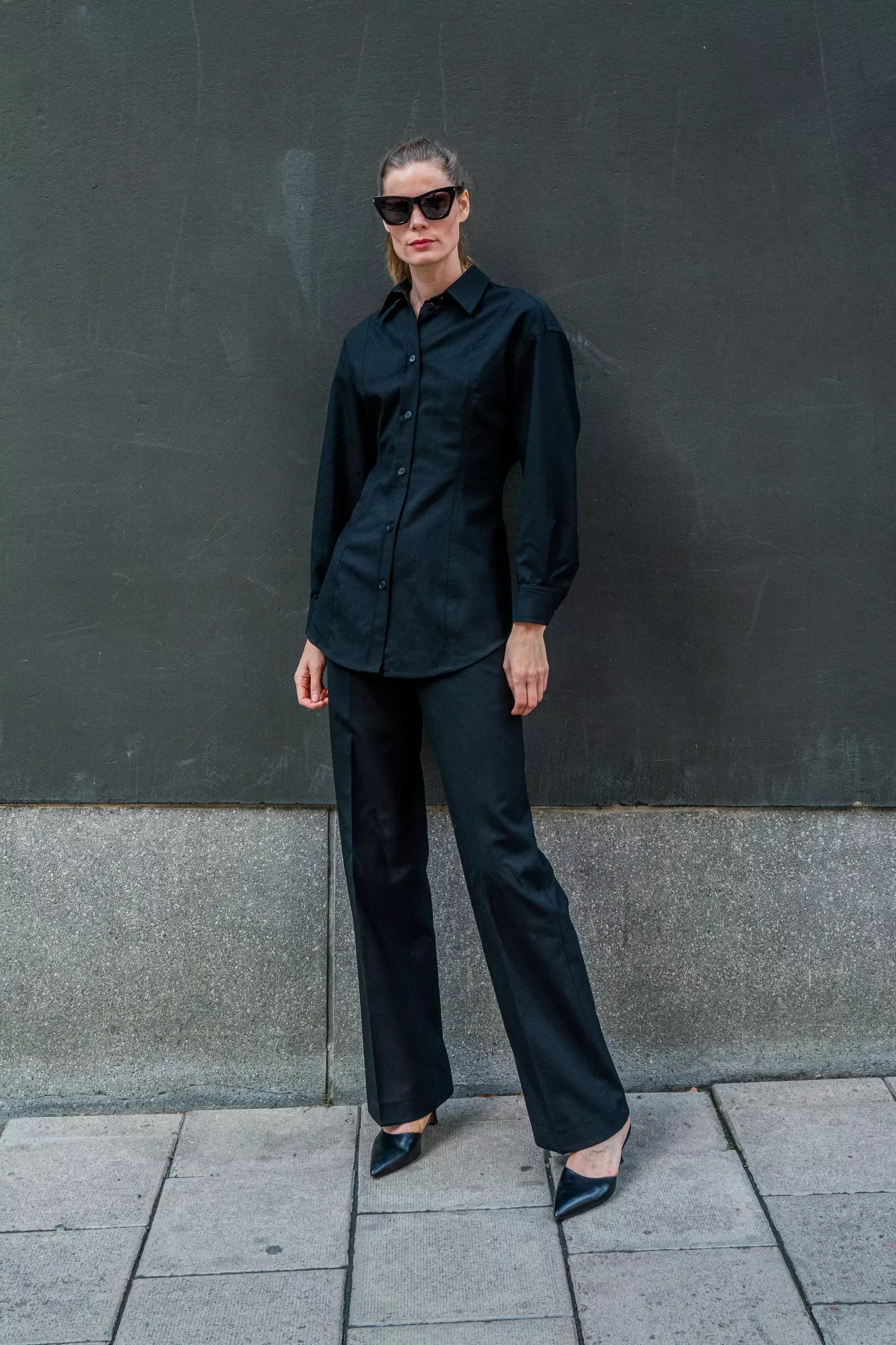 Stockholm Fashion Week guest pairs black blouse over black pants and heels 