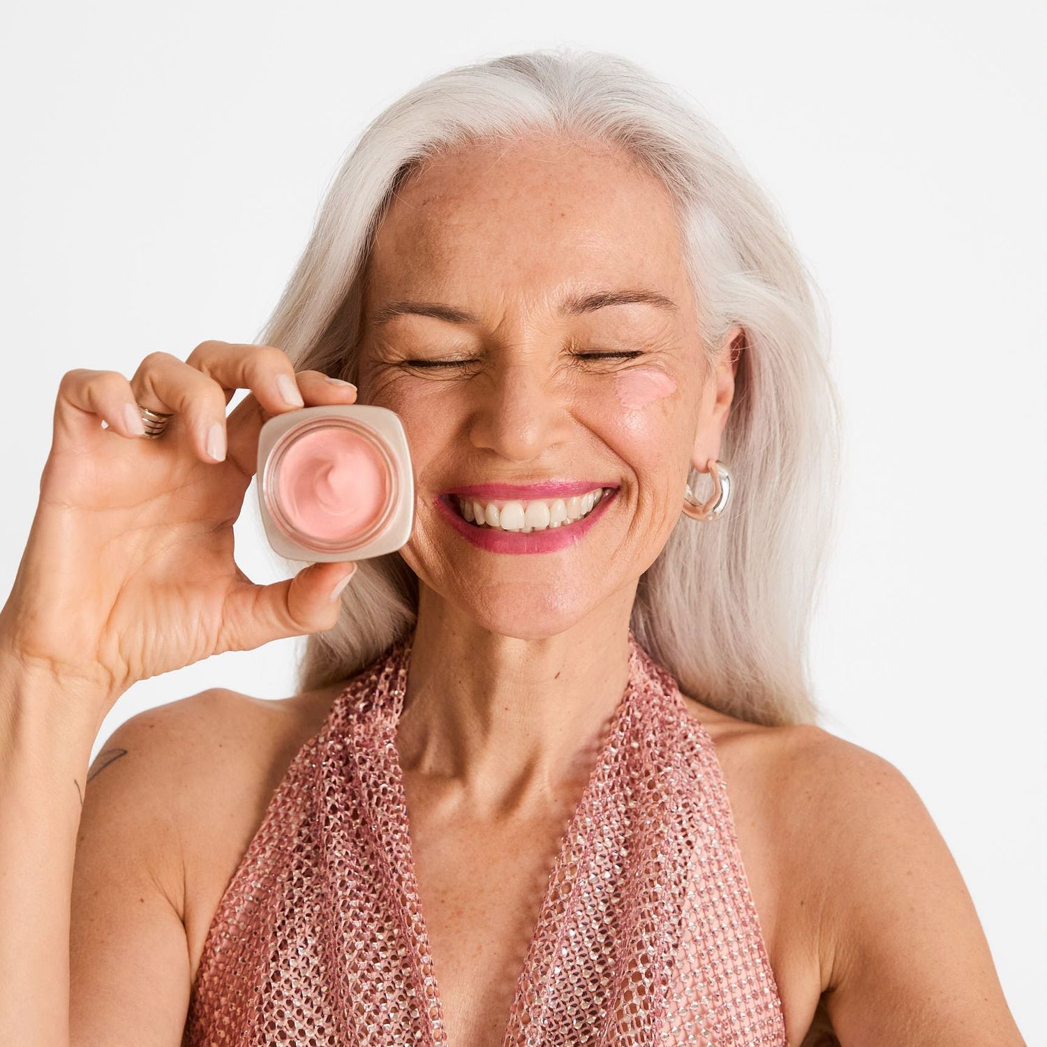 A mature model with white hair holds a rosy day cream 