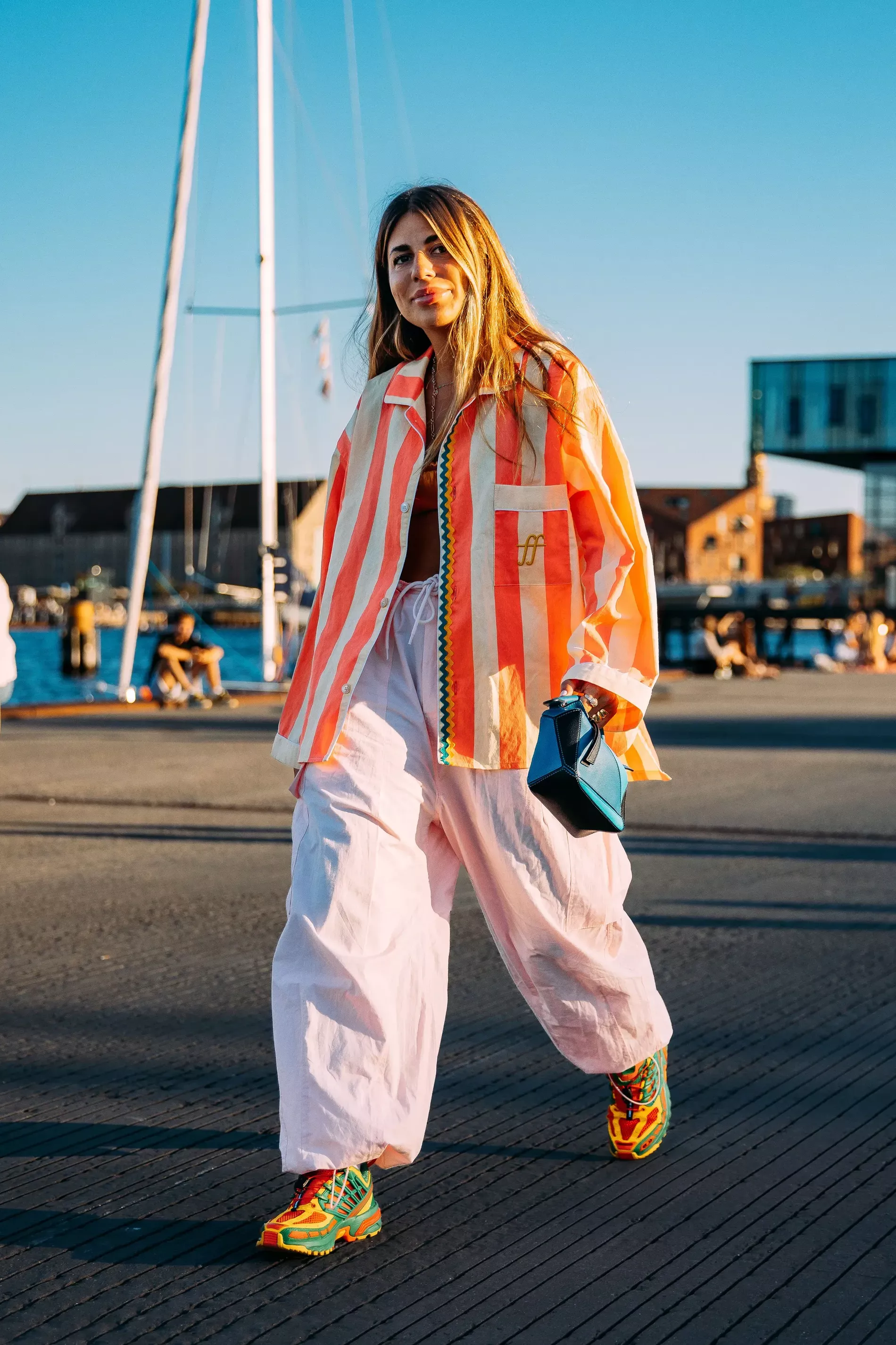 Copenhagen fashion week guest wears striped oversized shirt with pink pants and clutch